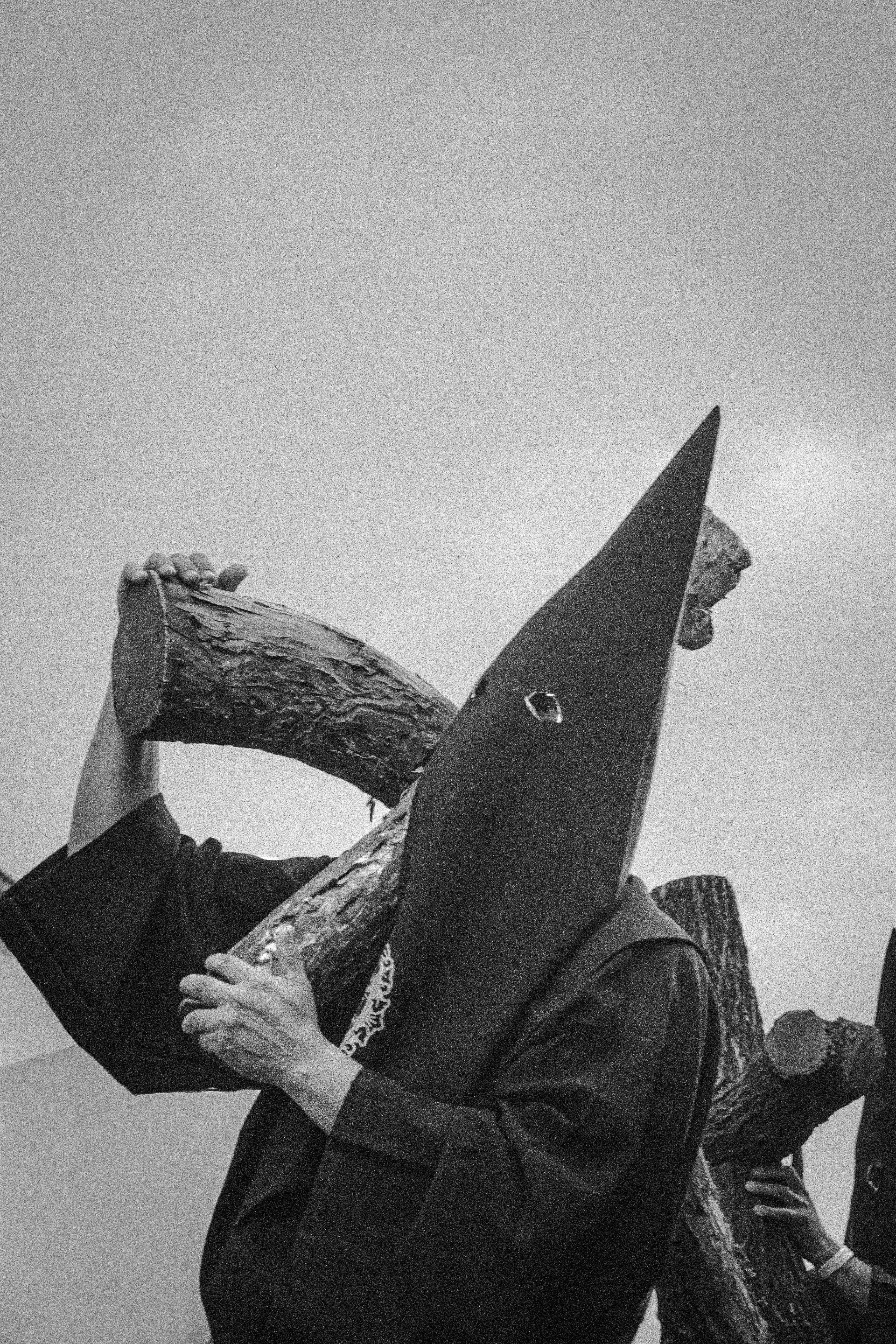 Person in hooded robe carries wooden cross