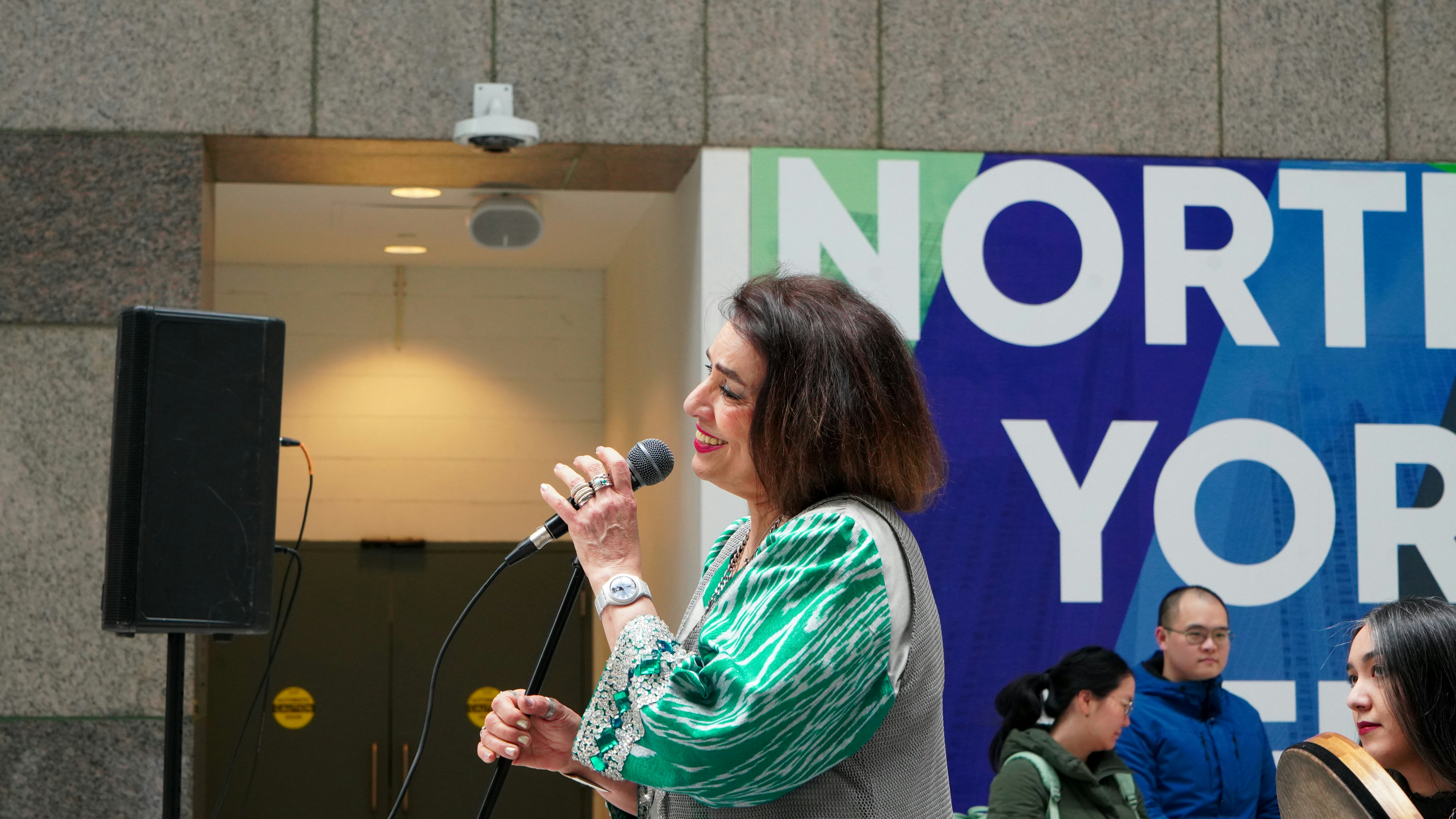 Woman singing into a microphone with a banner behind her