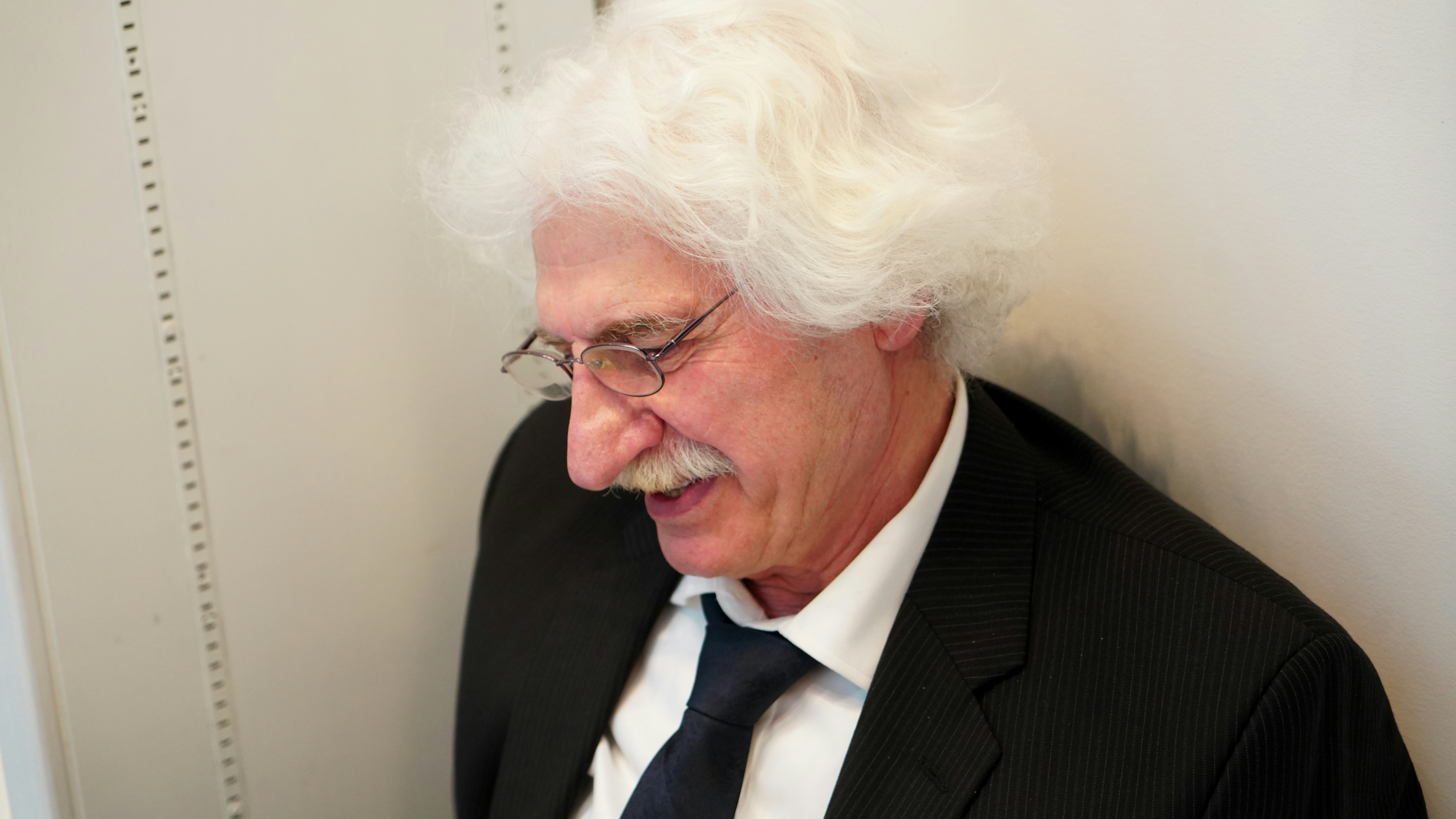Elderly man with white hair wearing a suit and tie.