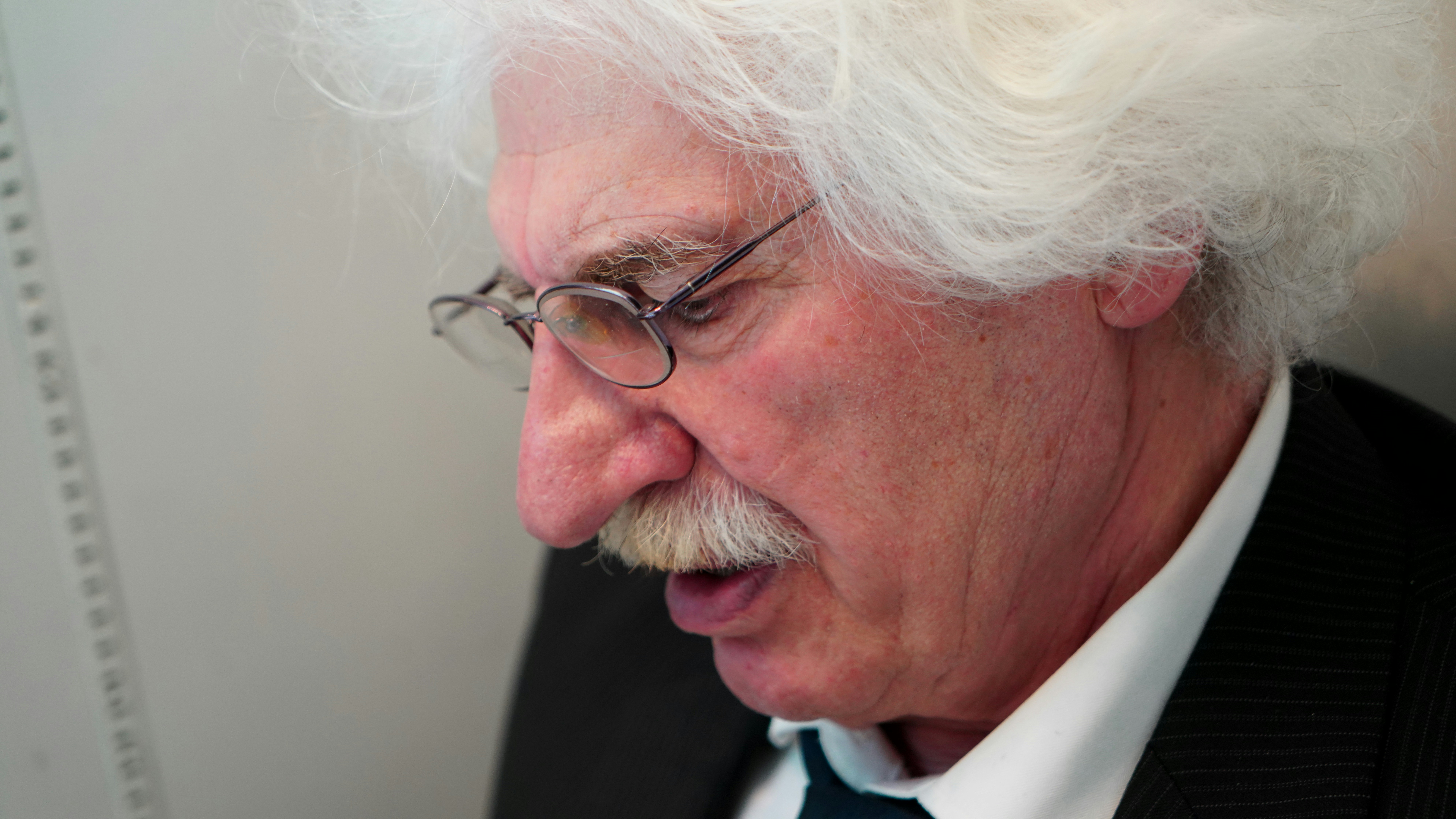 Elderly man with white hair and glasses speaking