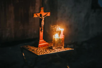 A crucifix and a lit candle on a table.