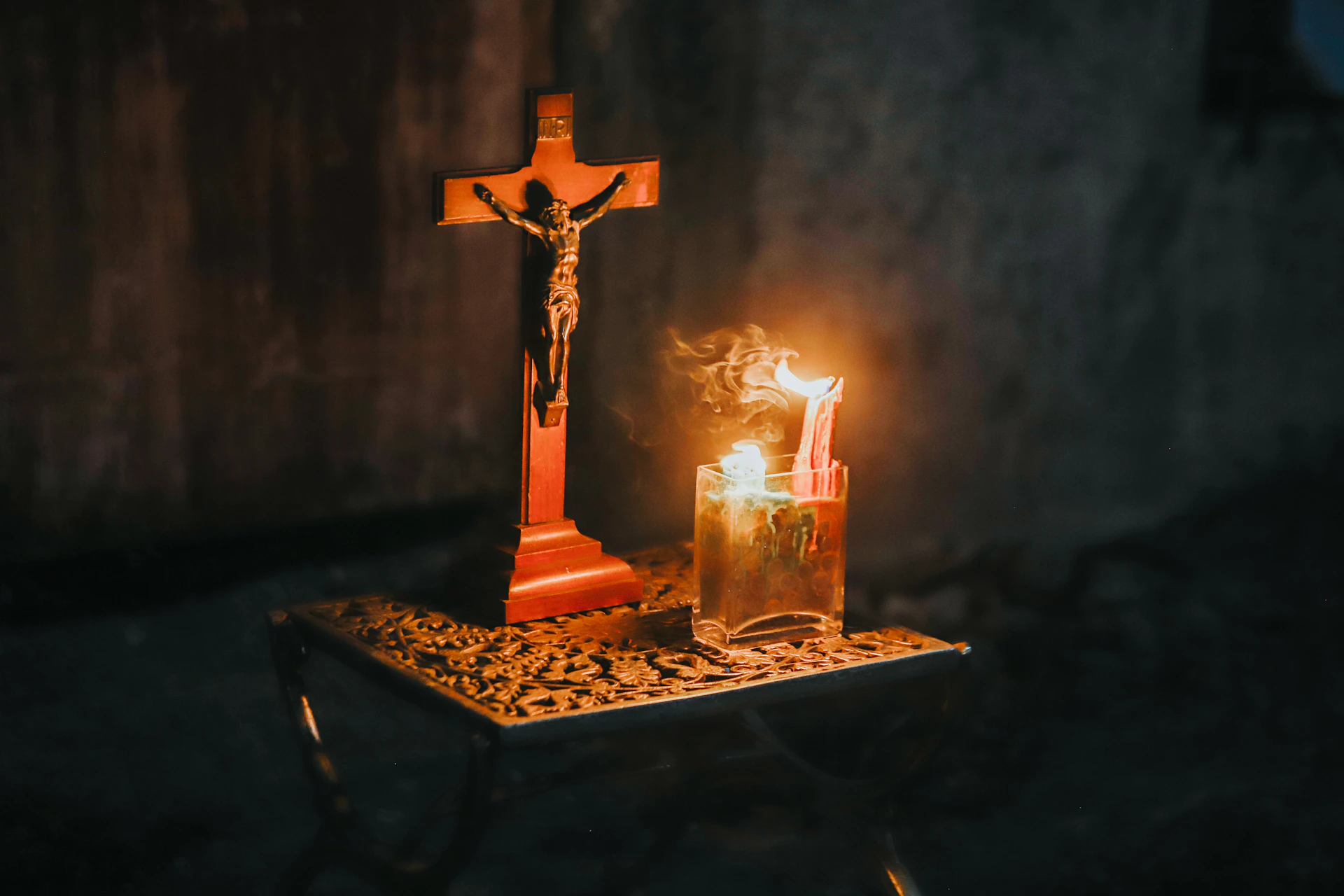 A crucifix and a lit candle on a table.