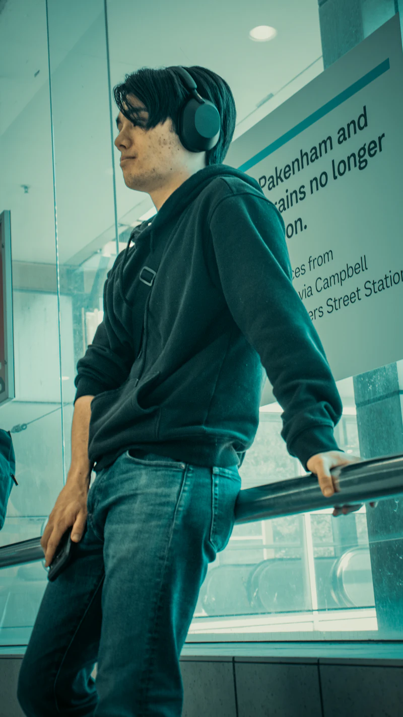 Un jeune homme avec un casque, appuyé à une rambarde de gare