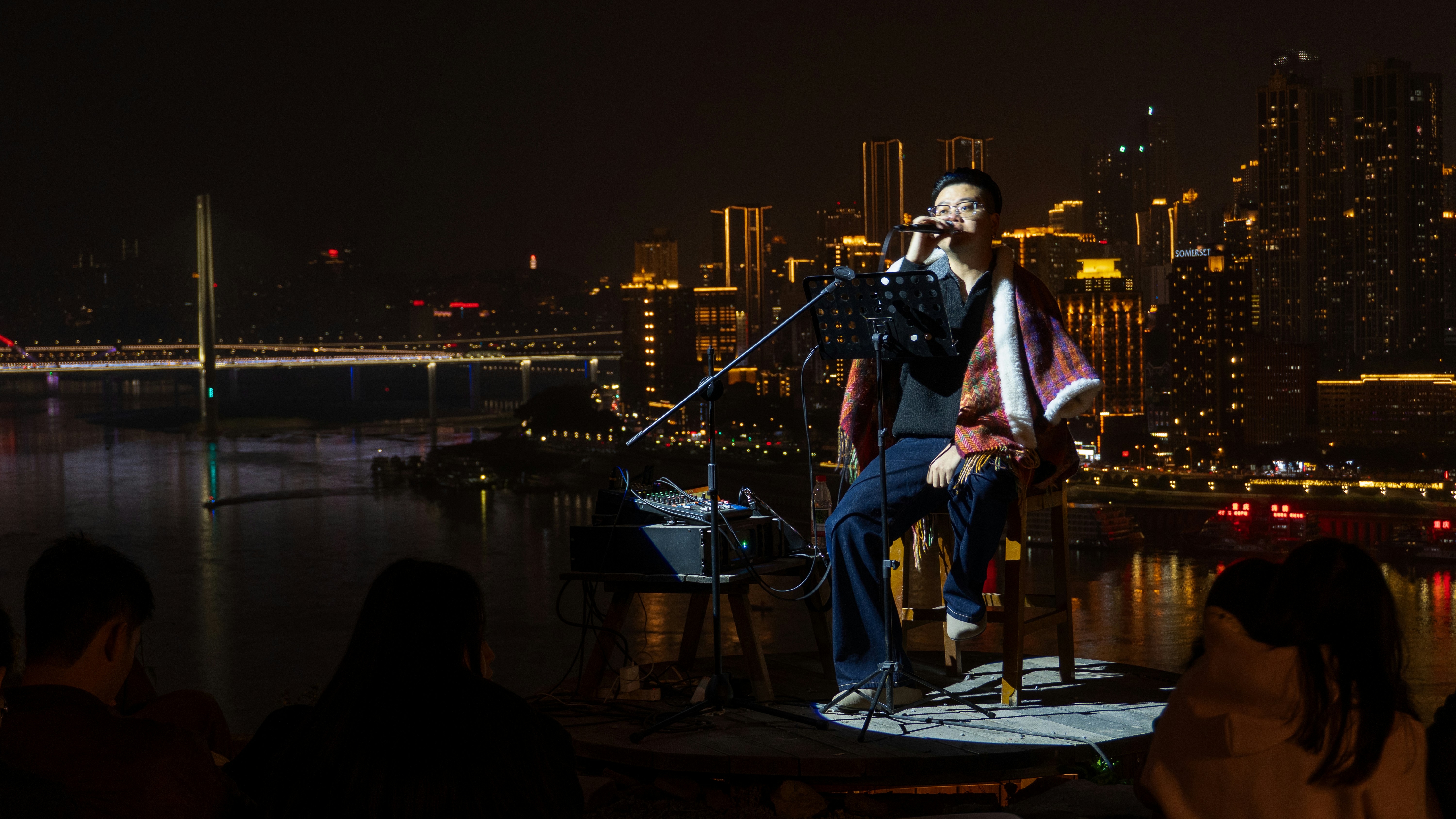Man singing on stage with city lights behind