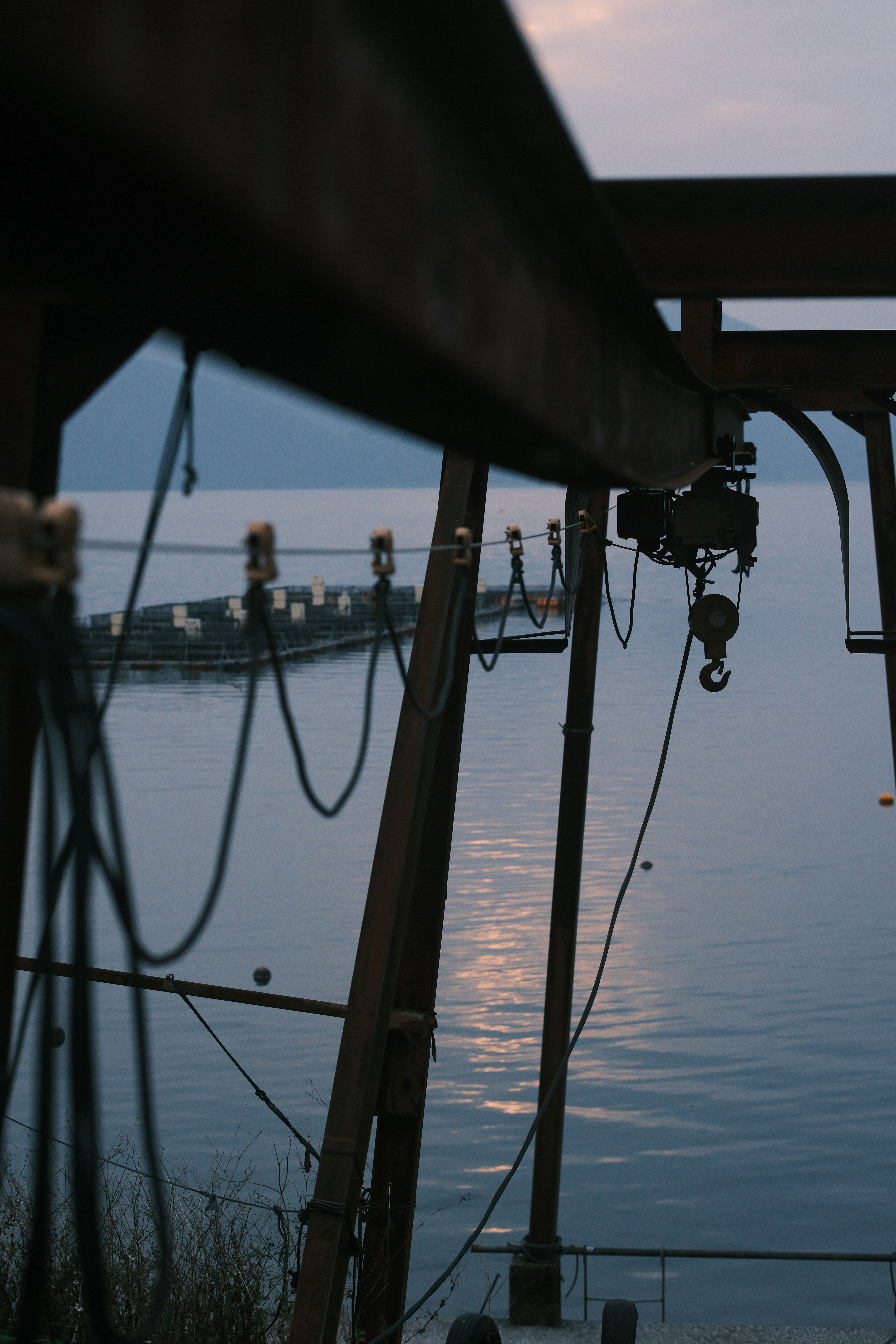 Rusty gantry crane by the calm ocean at dusk.