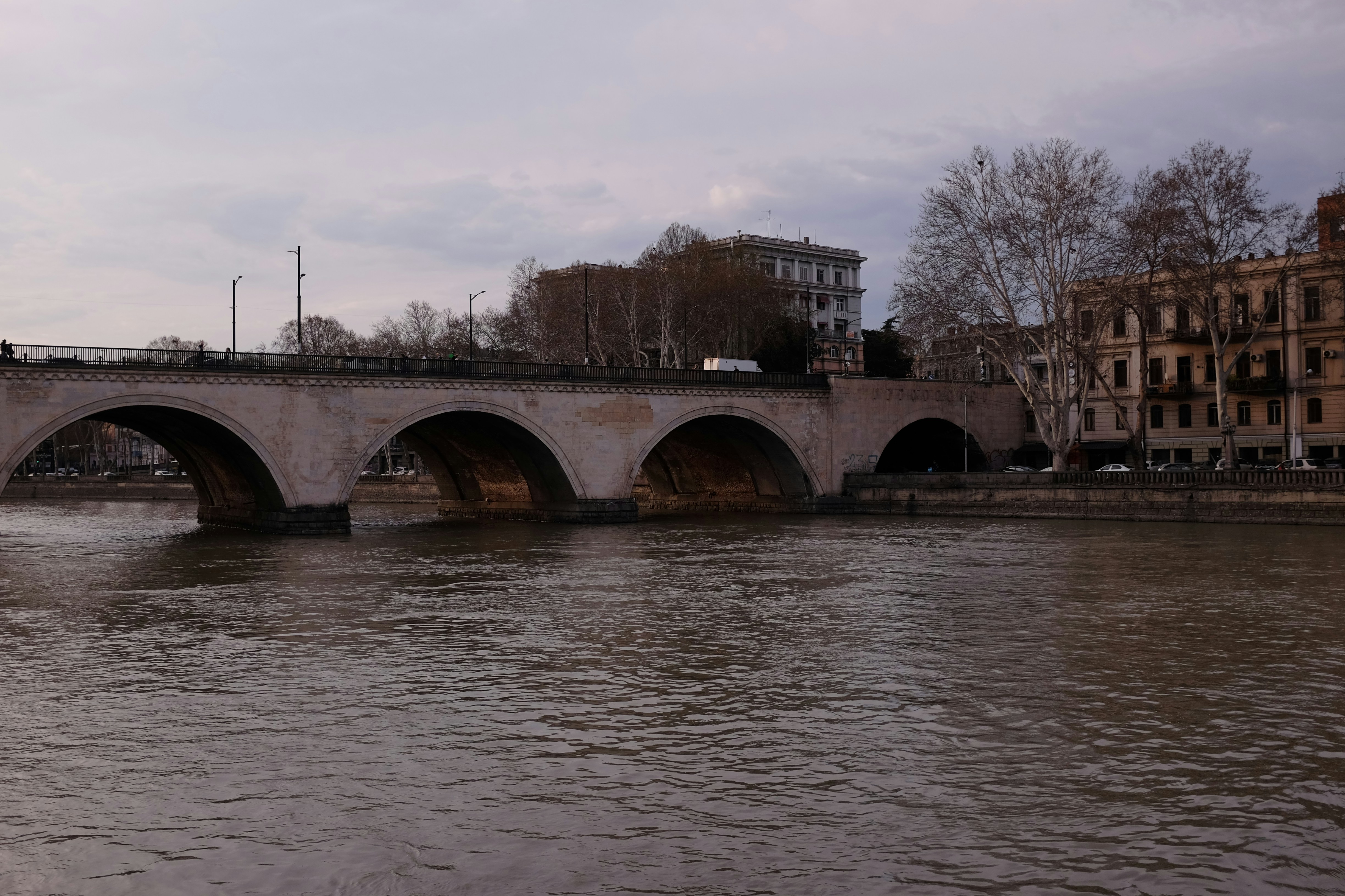Stone bridge crossing a wide river with buildings behind