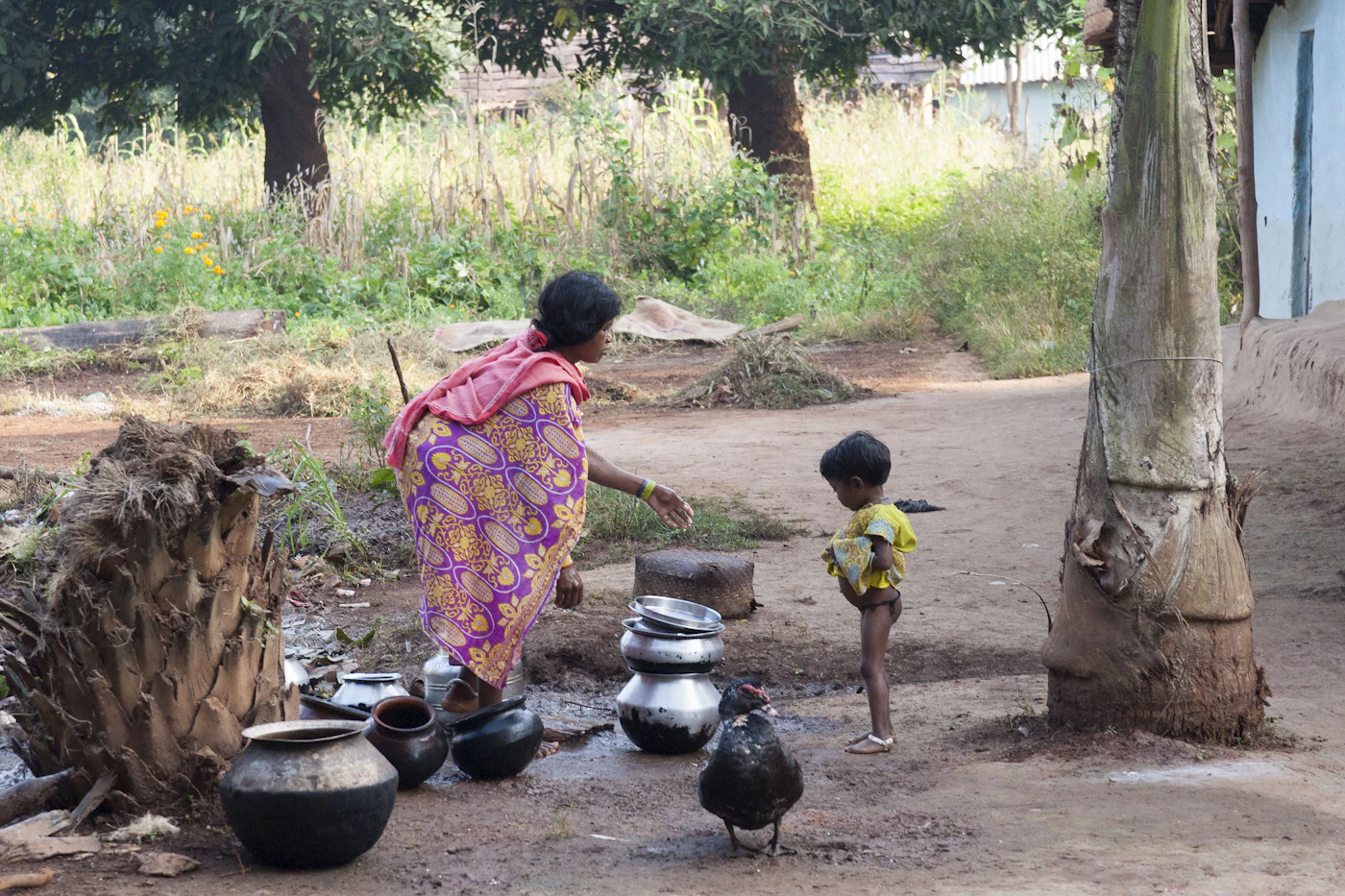 A woman and child with pots outside a rural home.