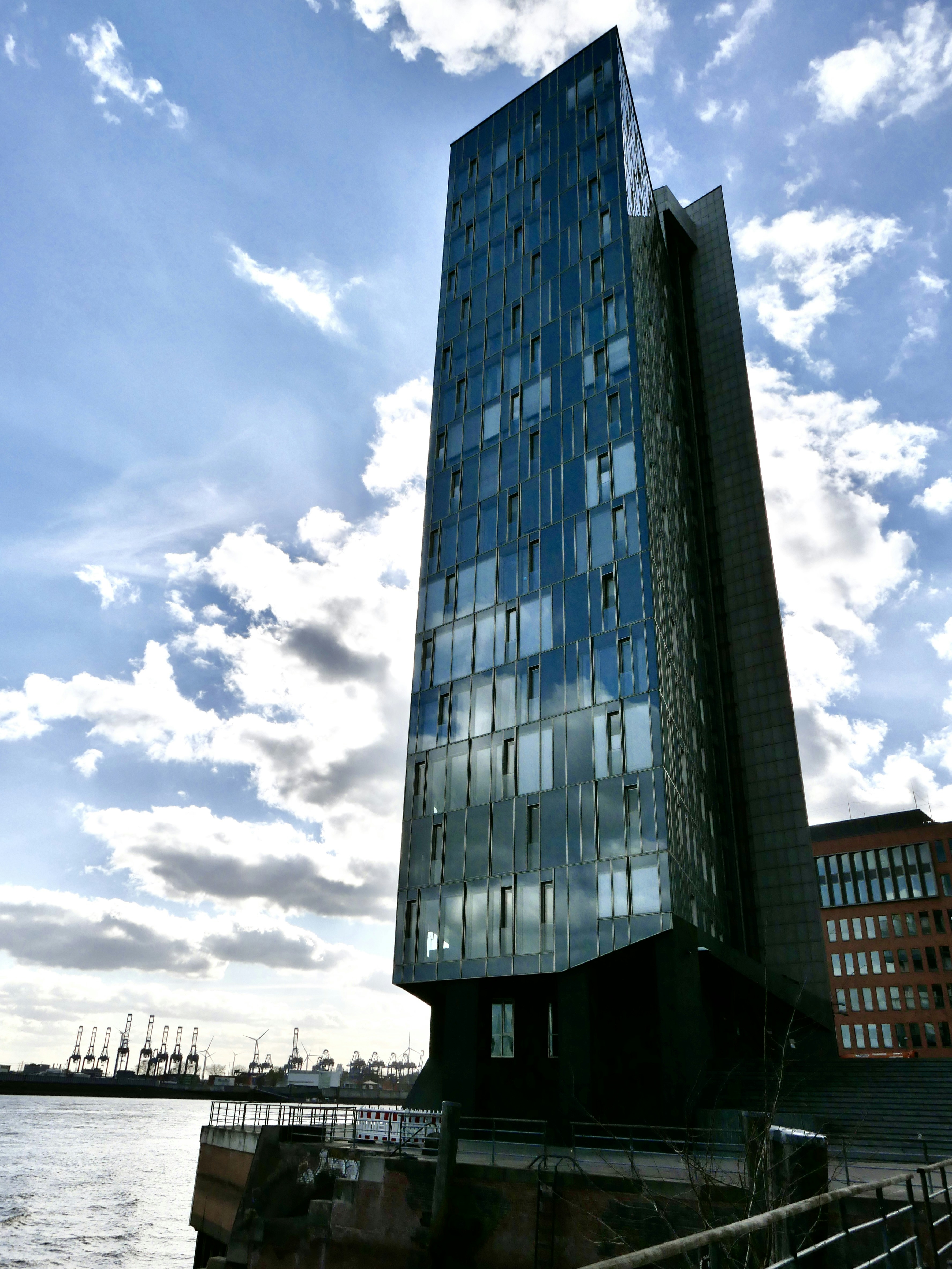 Modern glass skyscraper by the water under clouds