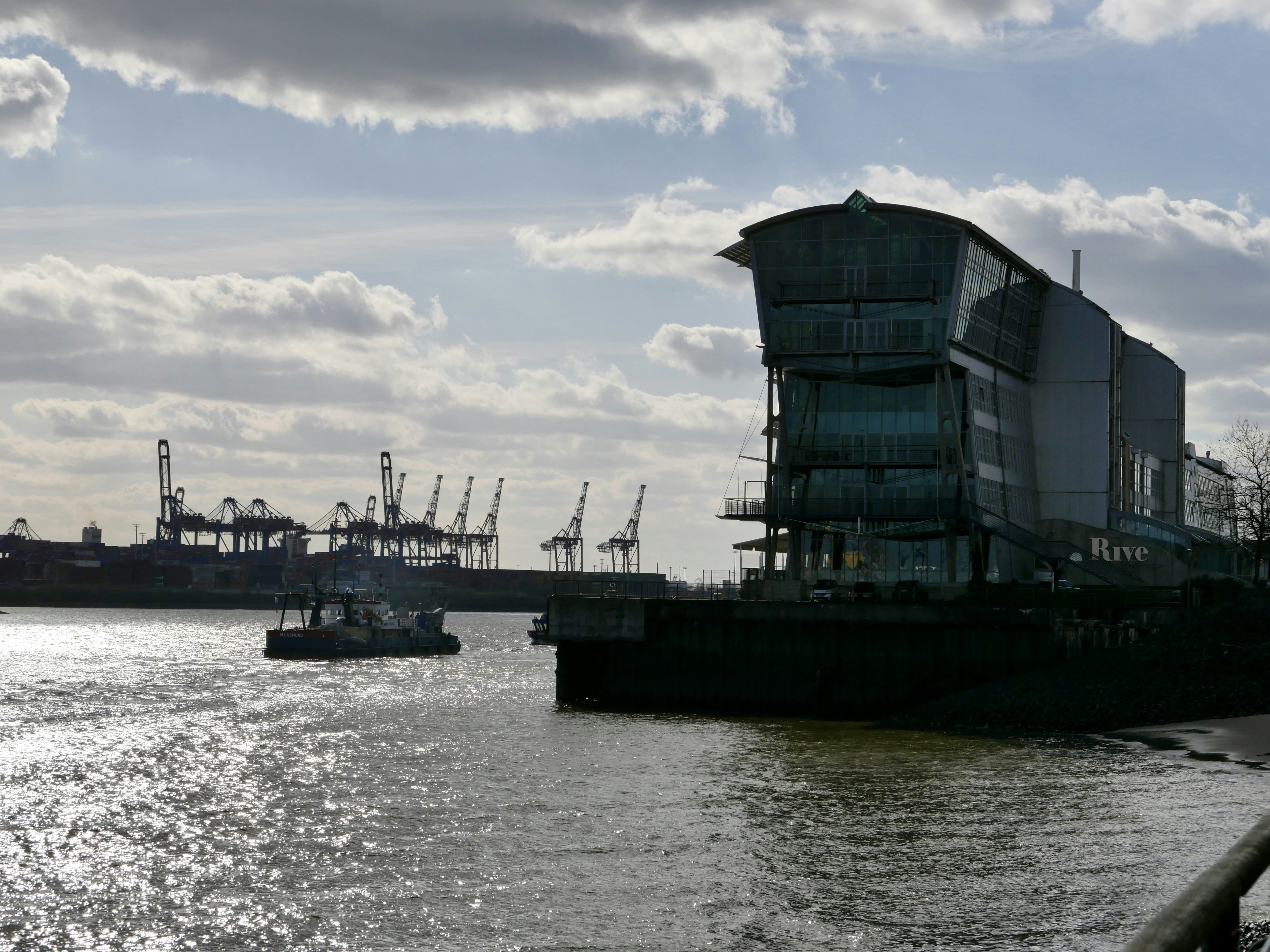 Modern building by a harbor with cranes and boat.