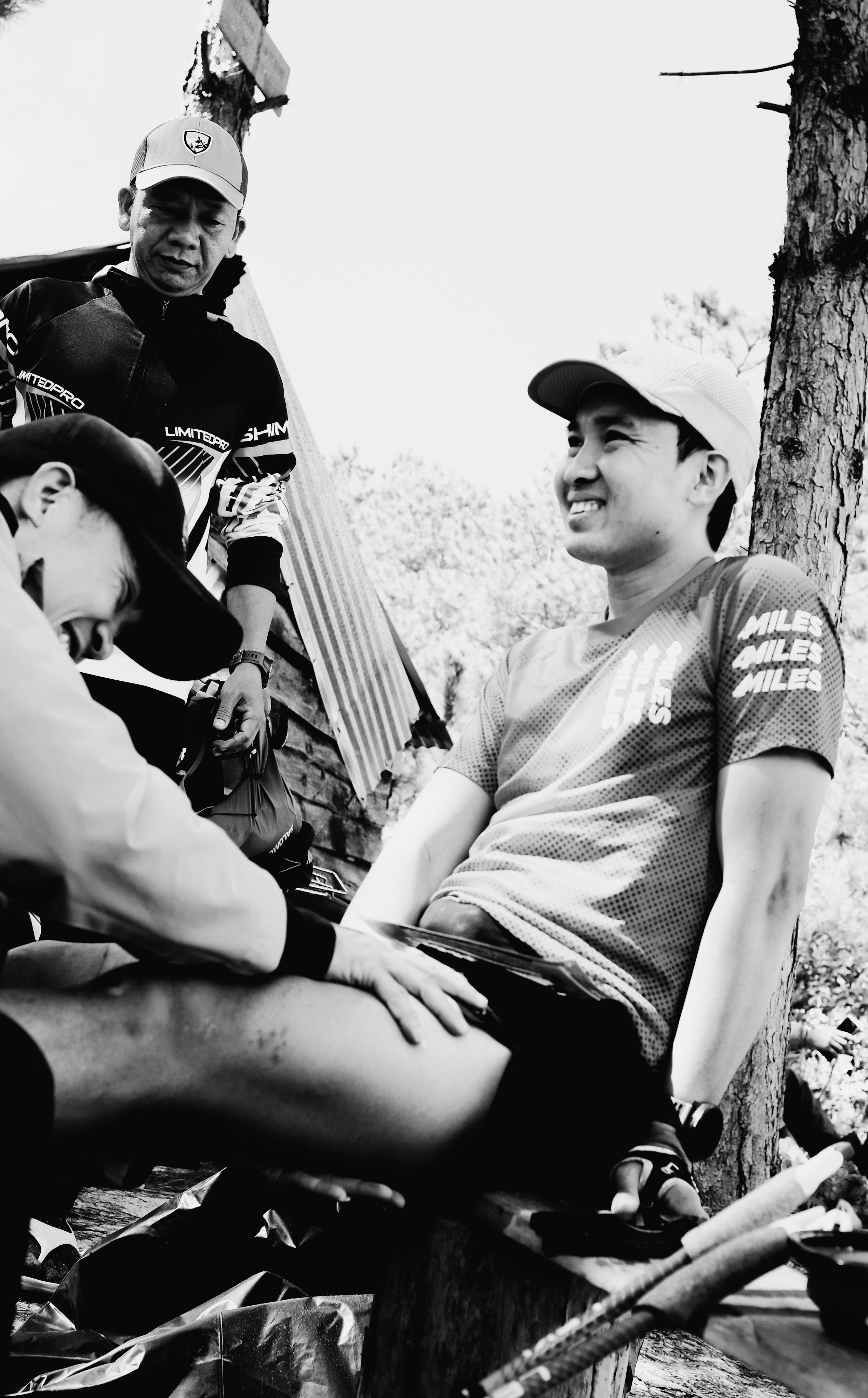 Three men resting outdoors, one receiving attention.