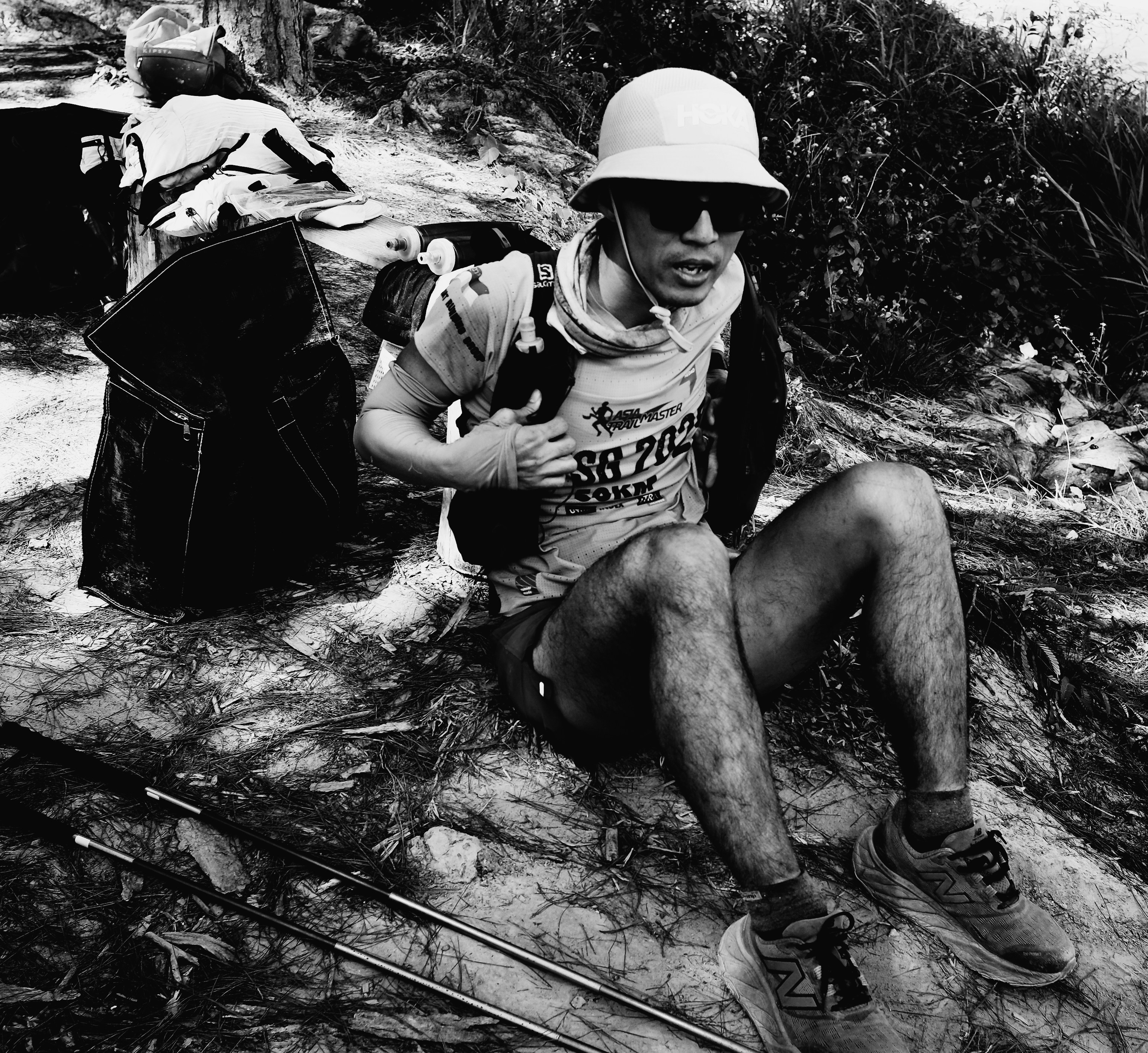 L'uomo con cappello e occhiali da sole siede sulle rocce con l'equipaggiamento