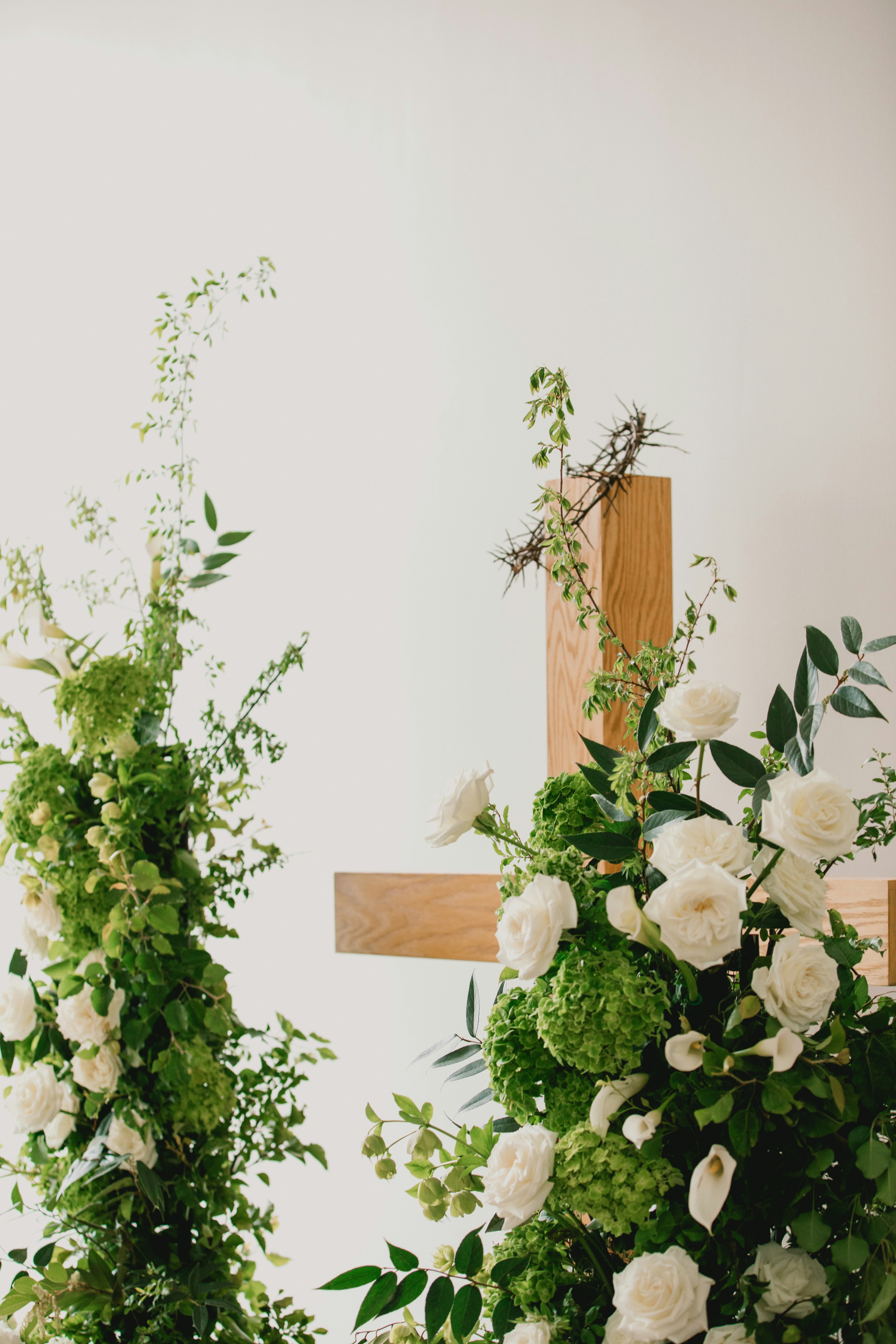 Wooden cross adorned with white roses and greenery