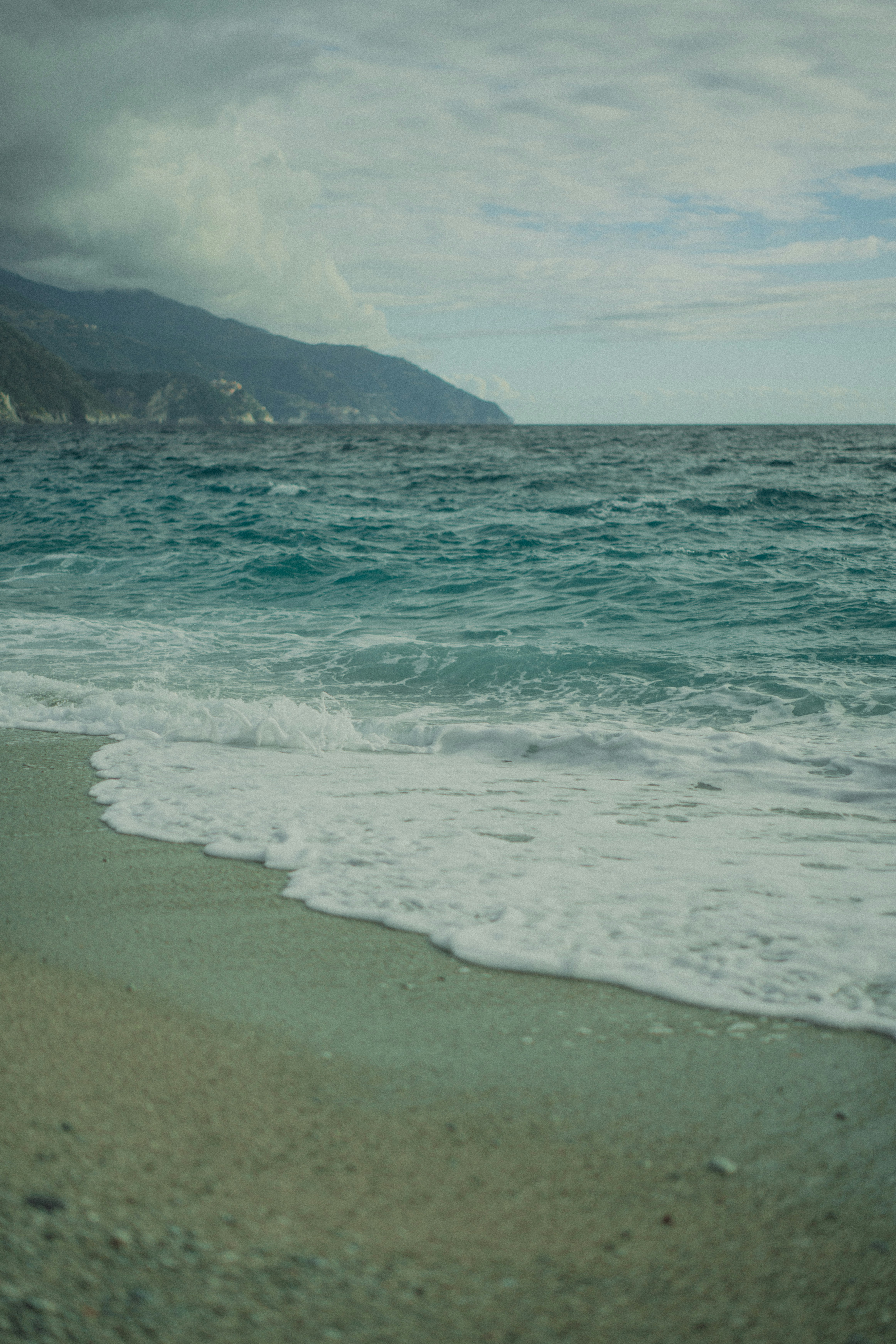 Waves gently crash on a rocky beach with mountains afar.