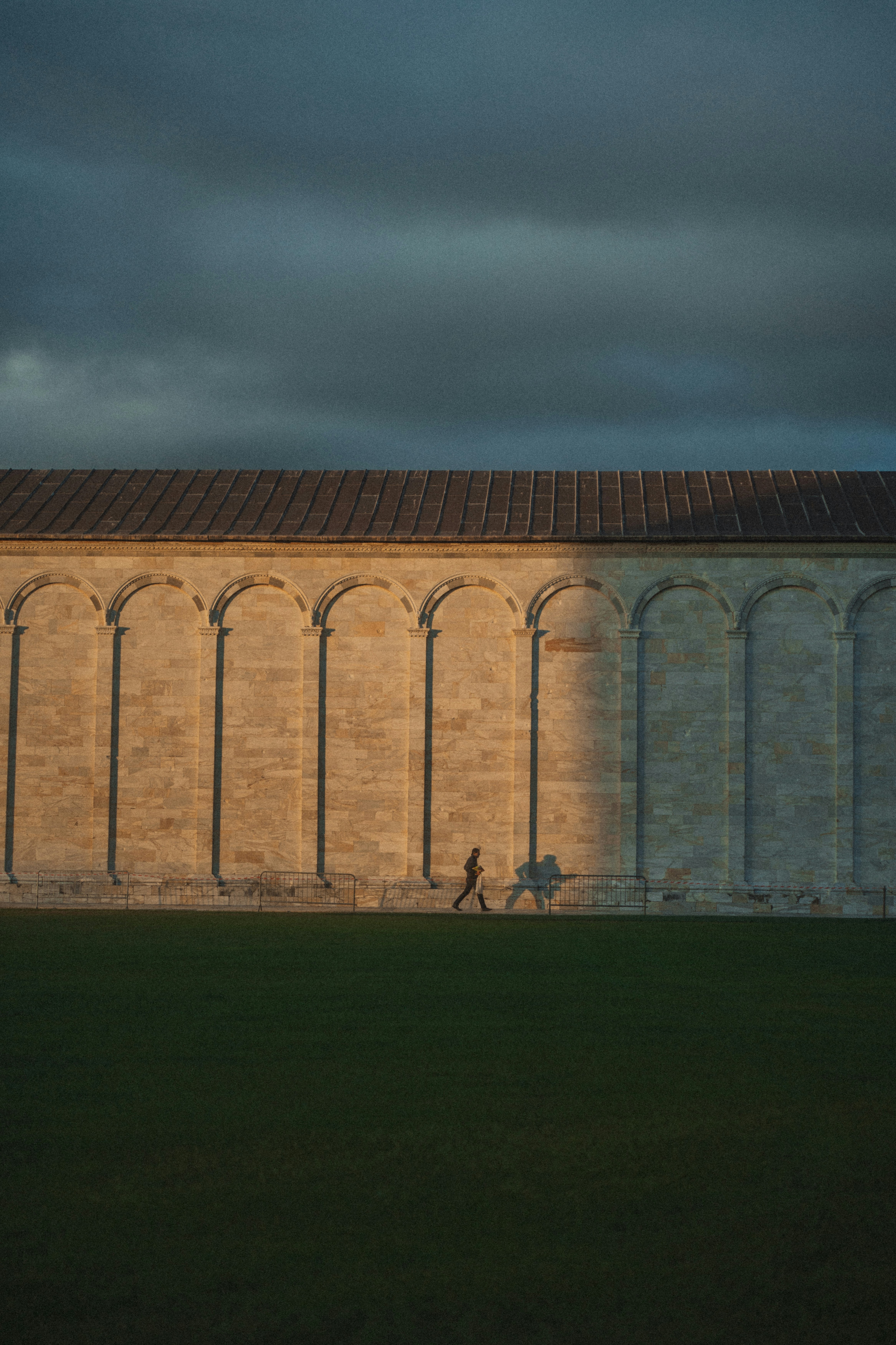 Person walking along a sunlit arched wall