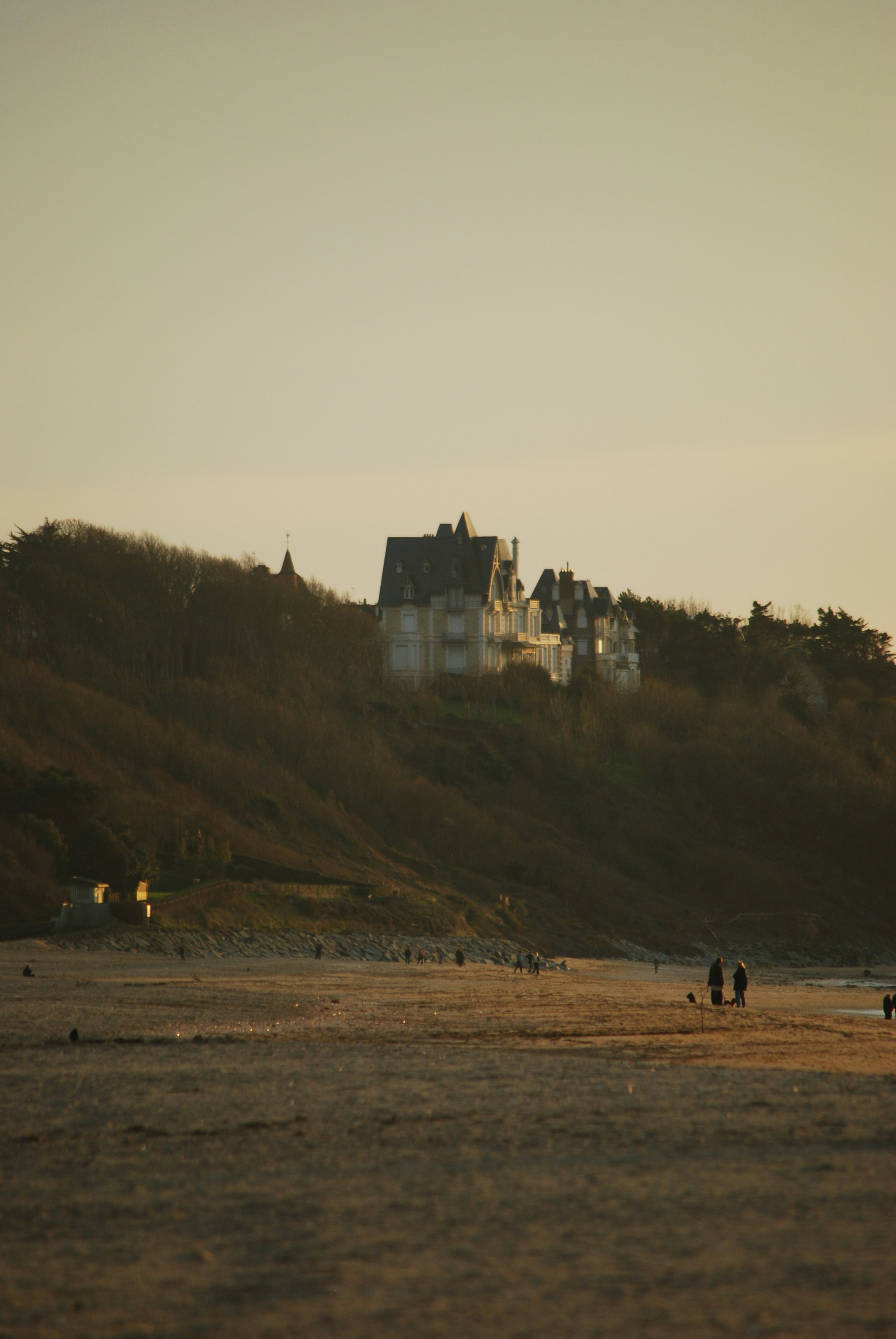 A large house sits atop a hill overlooking a beach.