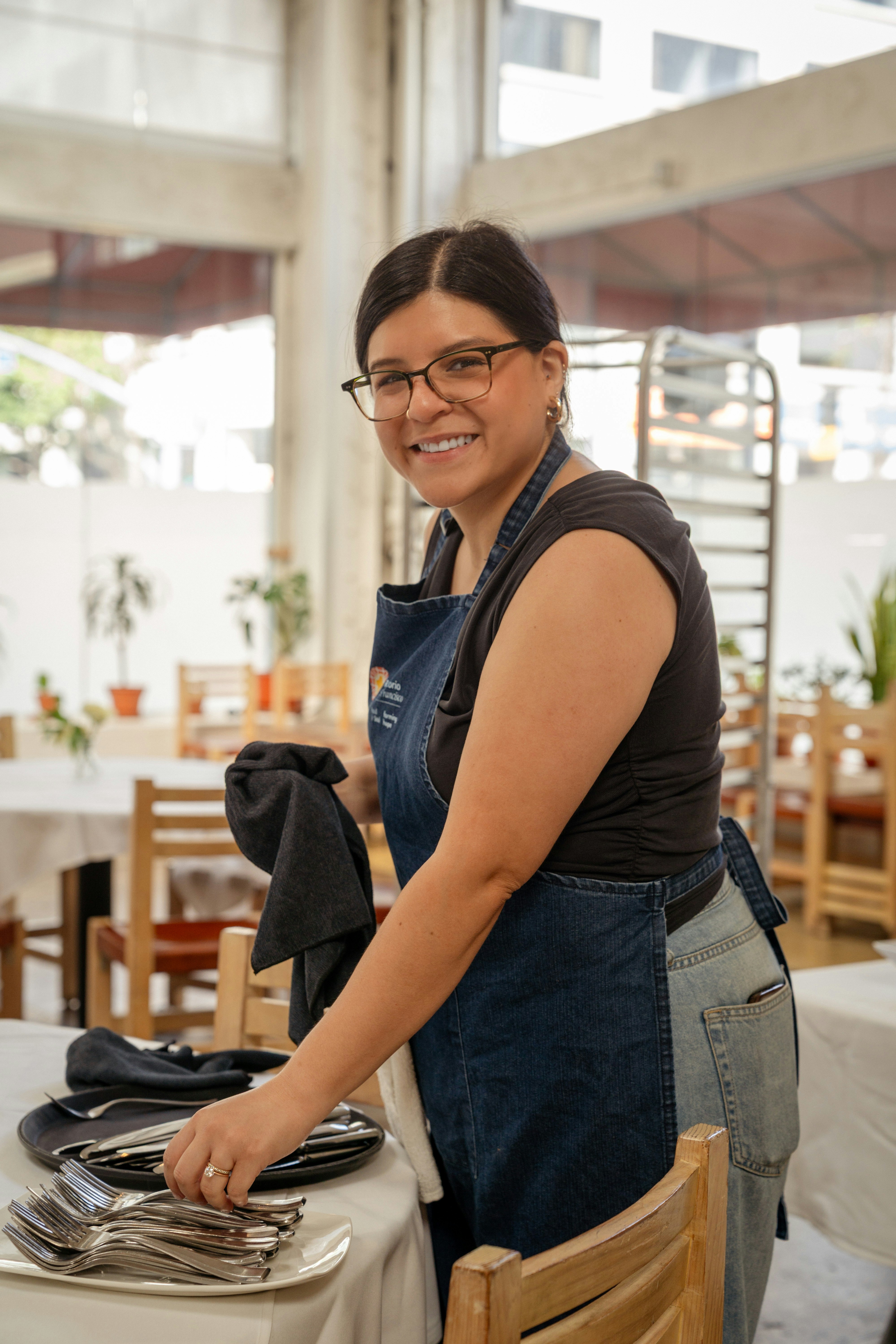 エプロンを着た女性が銀食器のテーブルを整えている。