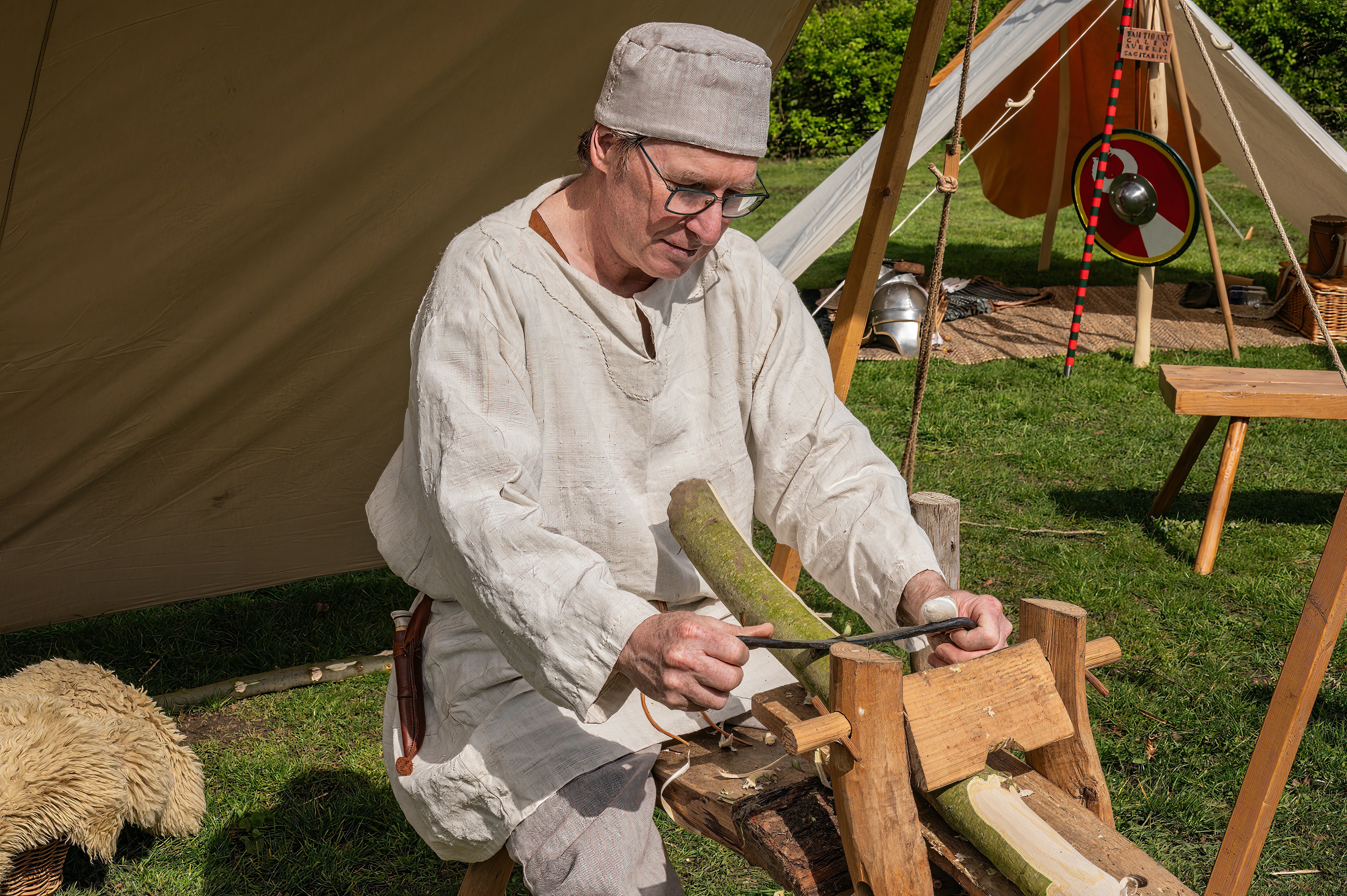 Man in historical clothing carves wood with a lathe
