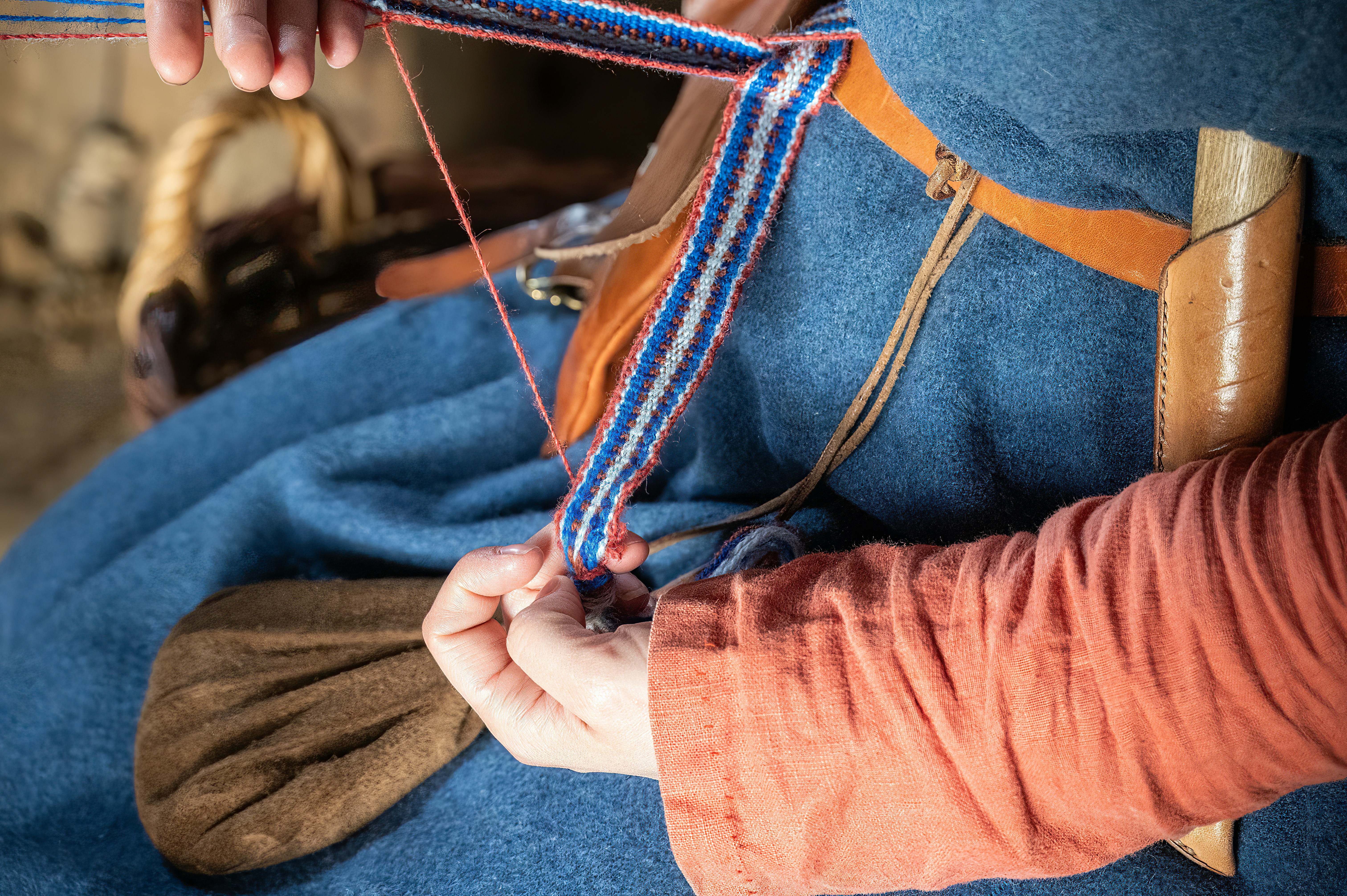 Hands weaving a colorful patterned fabric on a loom.