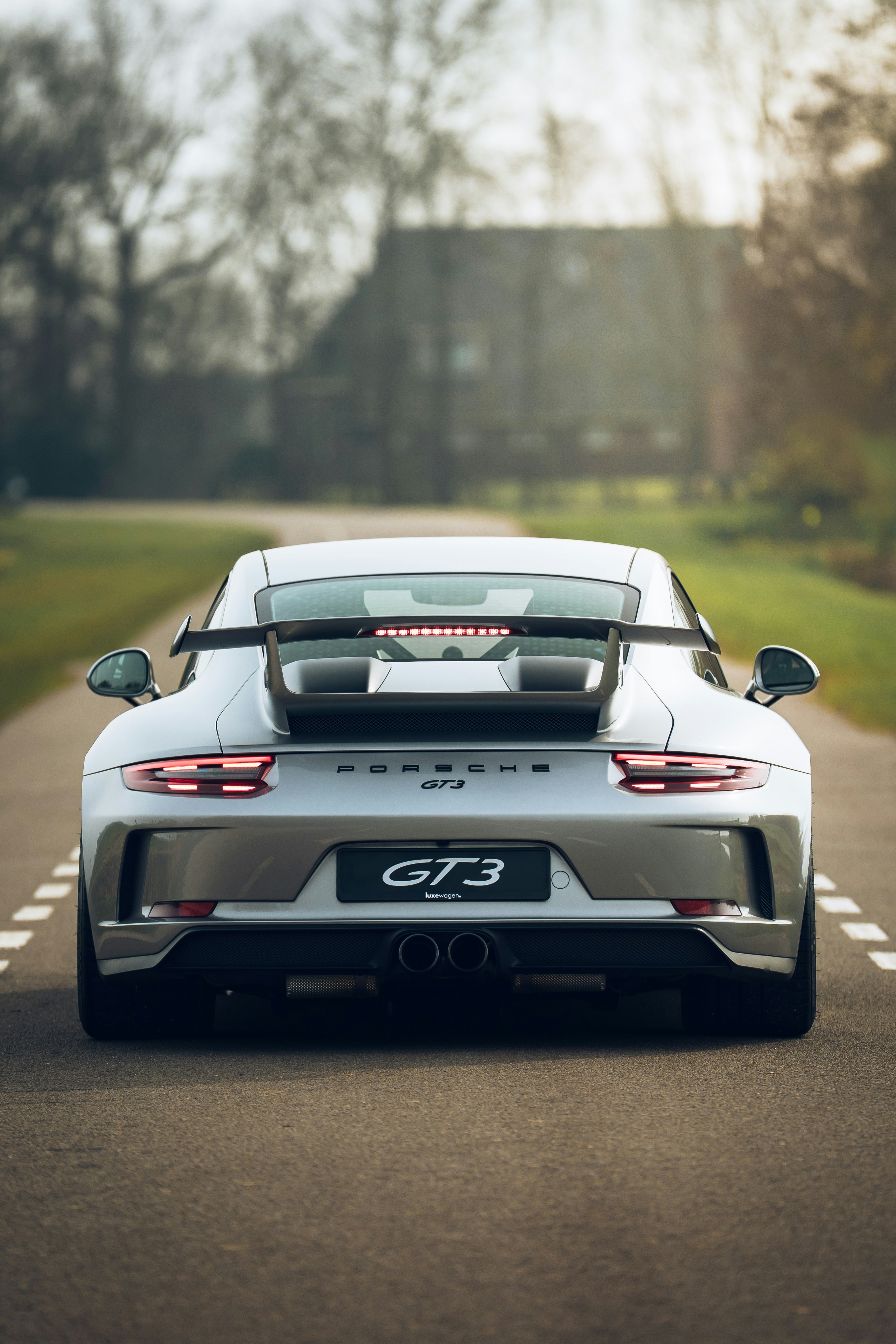 A silver porsche gt3 drives down a rural road