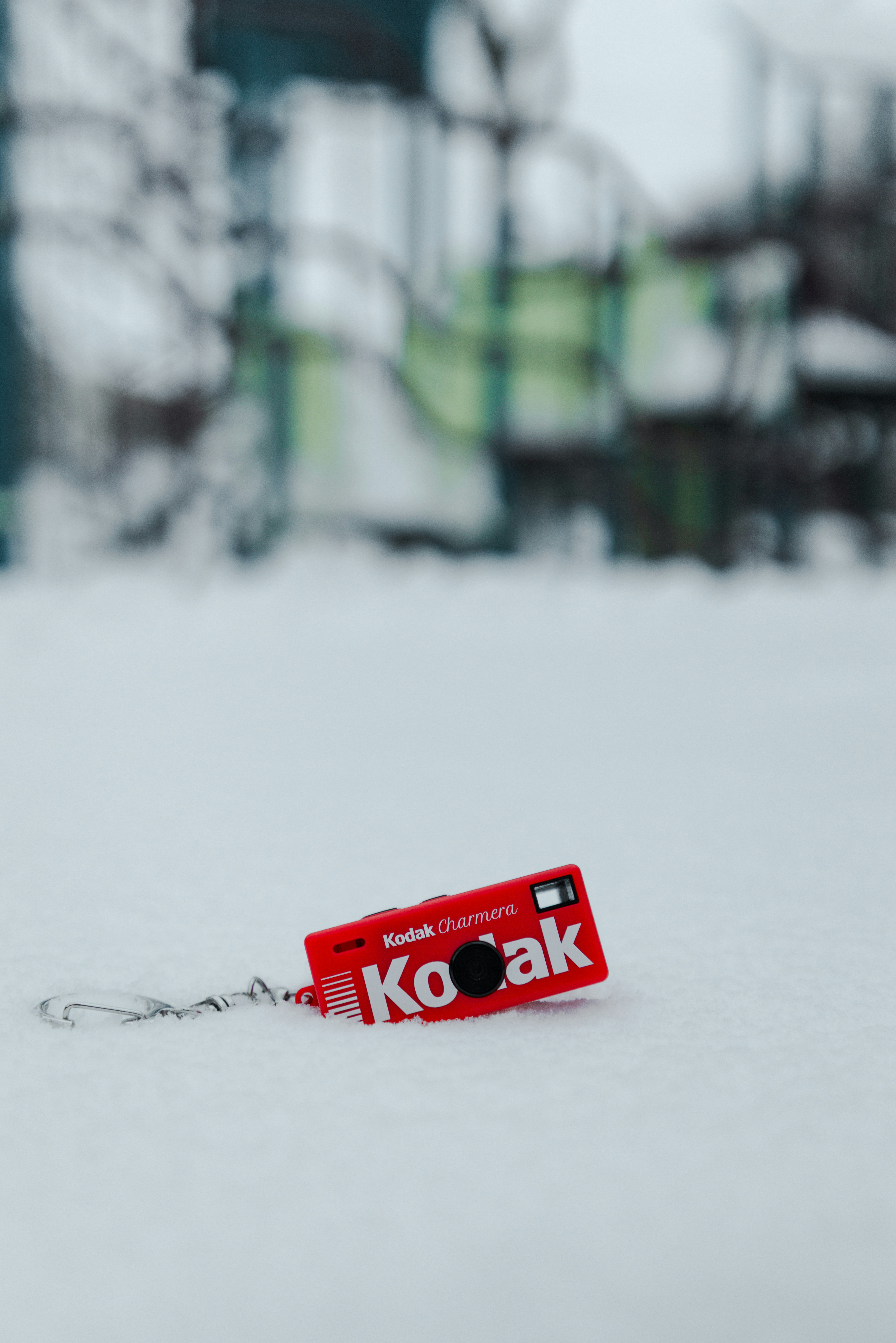 Un pequeño llavero rojo de cámara Kodak descansa sobre la nieve.