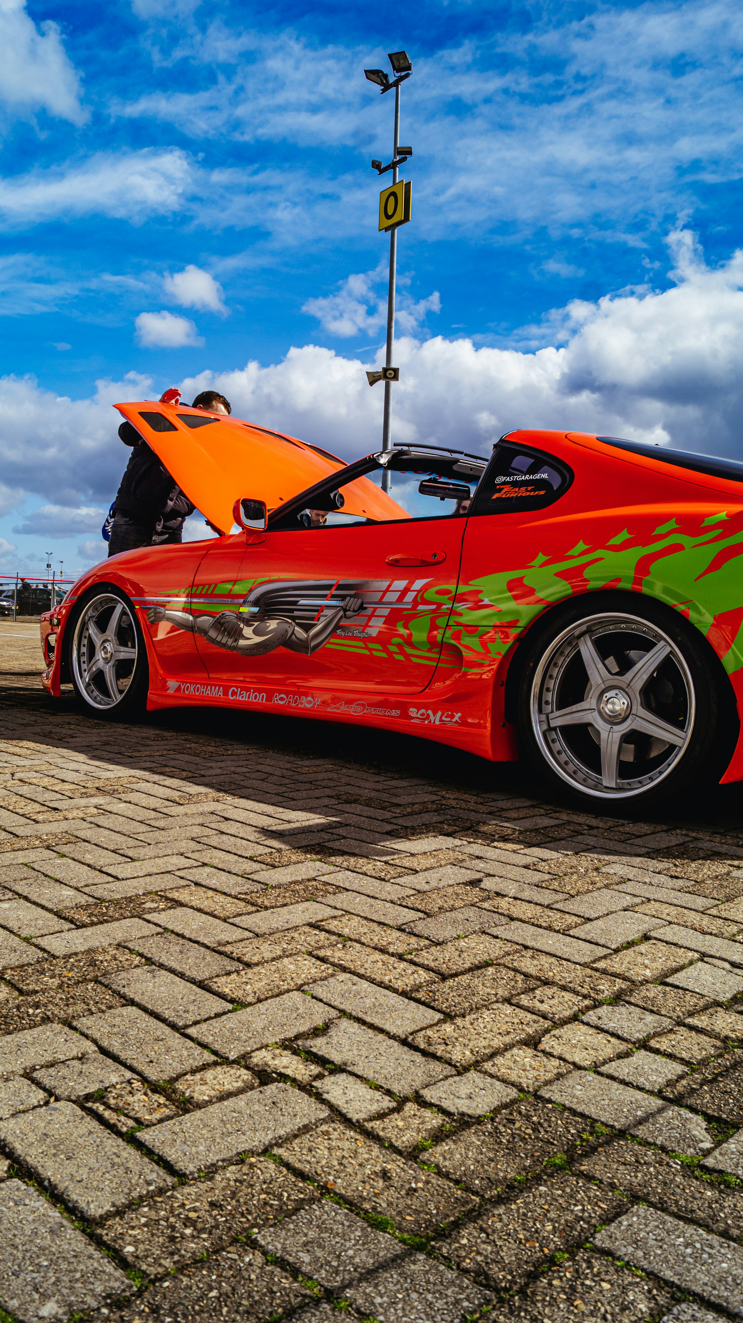 Orange sports car with green decals parked on pavement