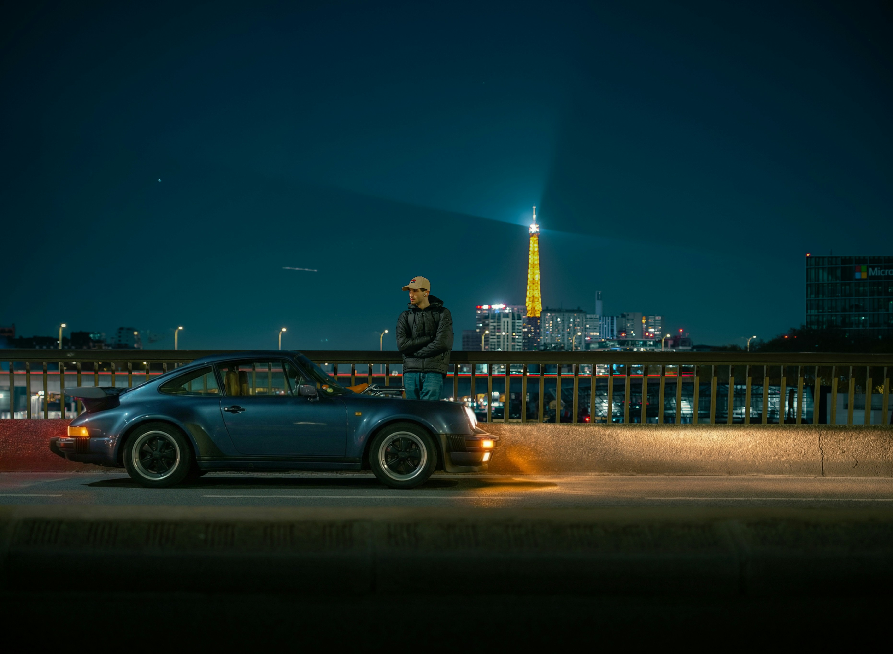 Un homme appuyé sur une voiture classique avec la tour Eiffel la nuit