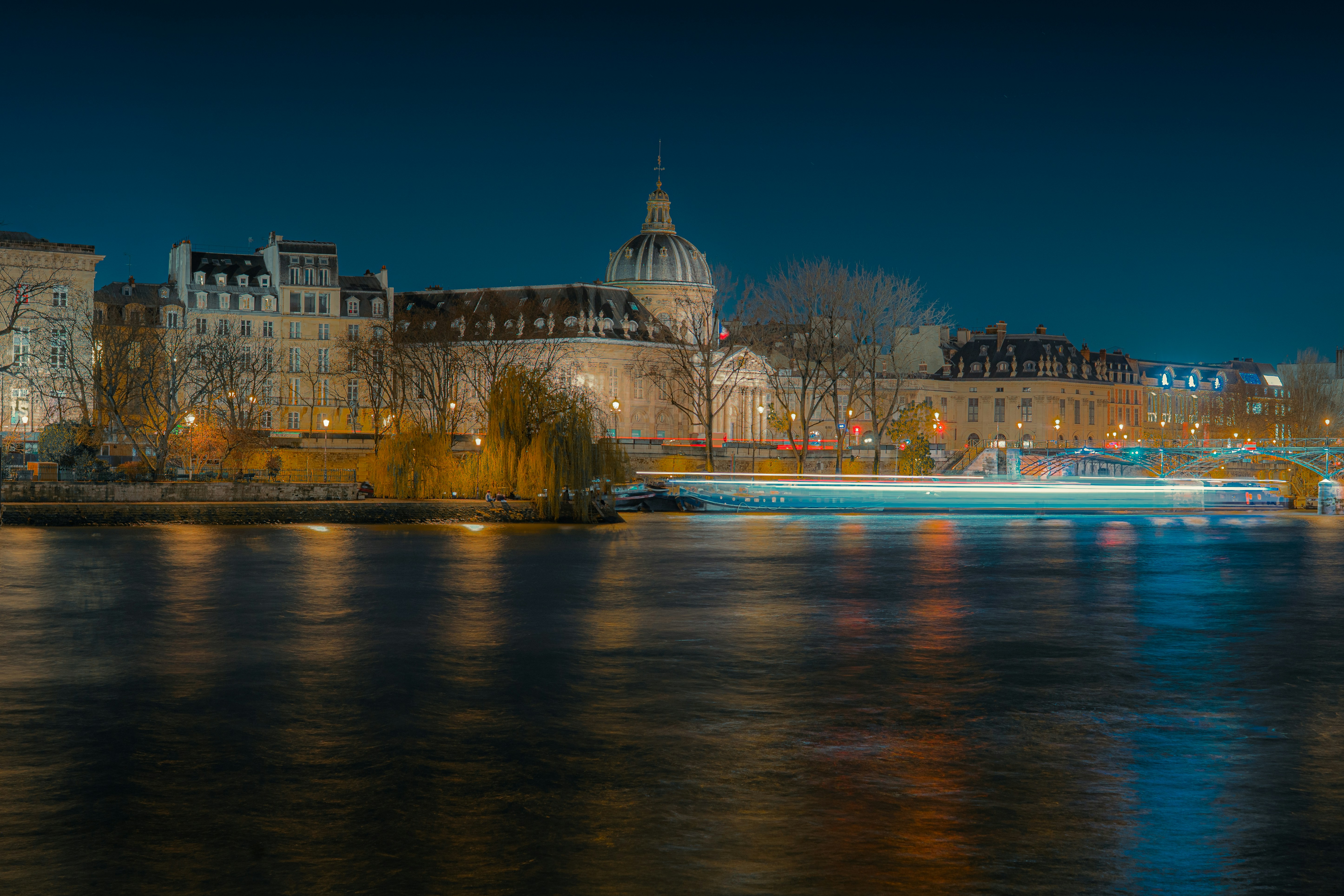 Paysage urbain avec des bâtiments illuminés et une rivière la nuit.