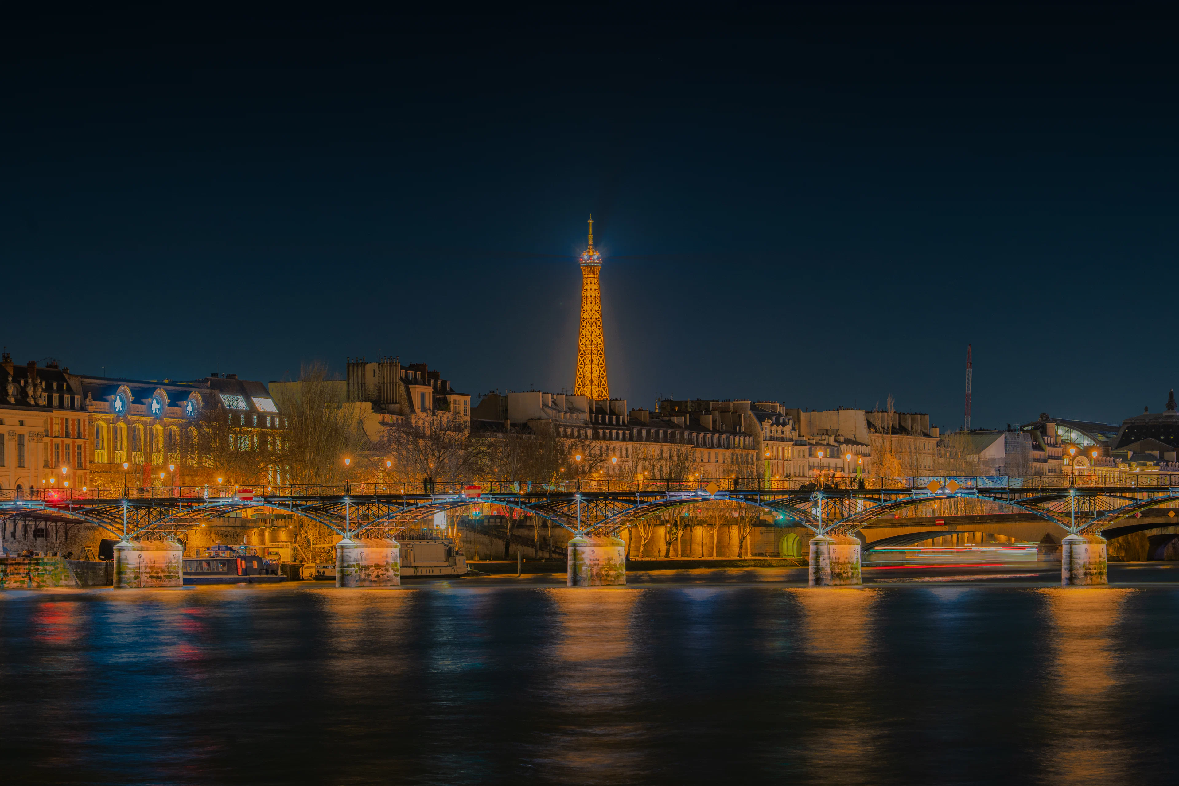 The illuminated Eiffel Tower at night above the Seine and the Pont des Arts