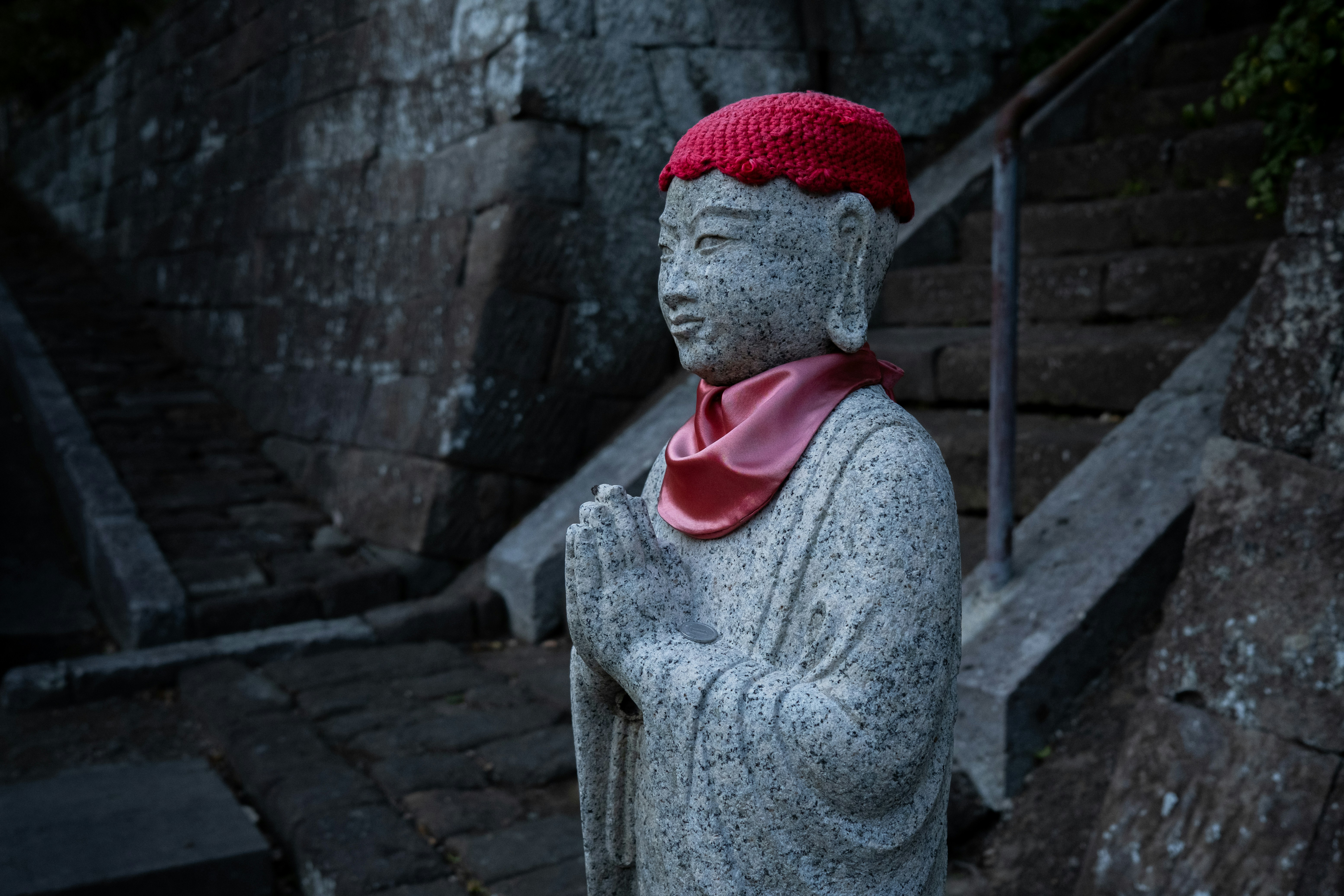 Statue de pierre avec un chapeau rouge et une écharpe rose priant.
