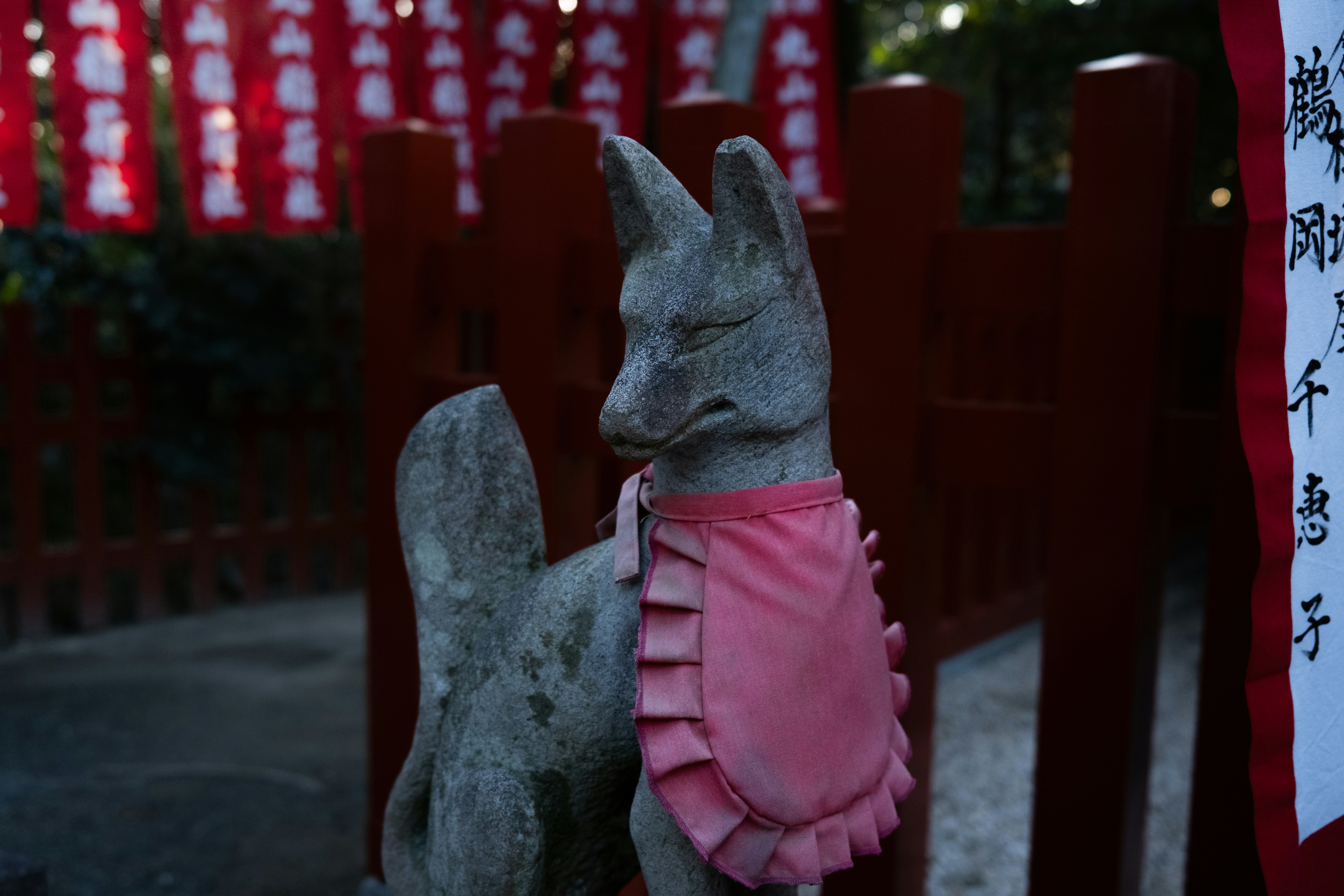 Statue de renard de pierre portant un bavoir rose au sanctuaire.