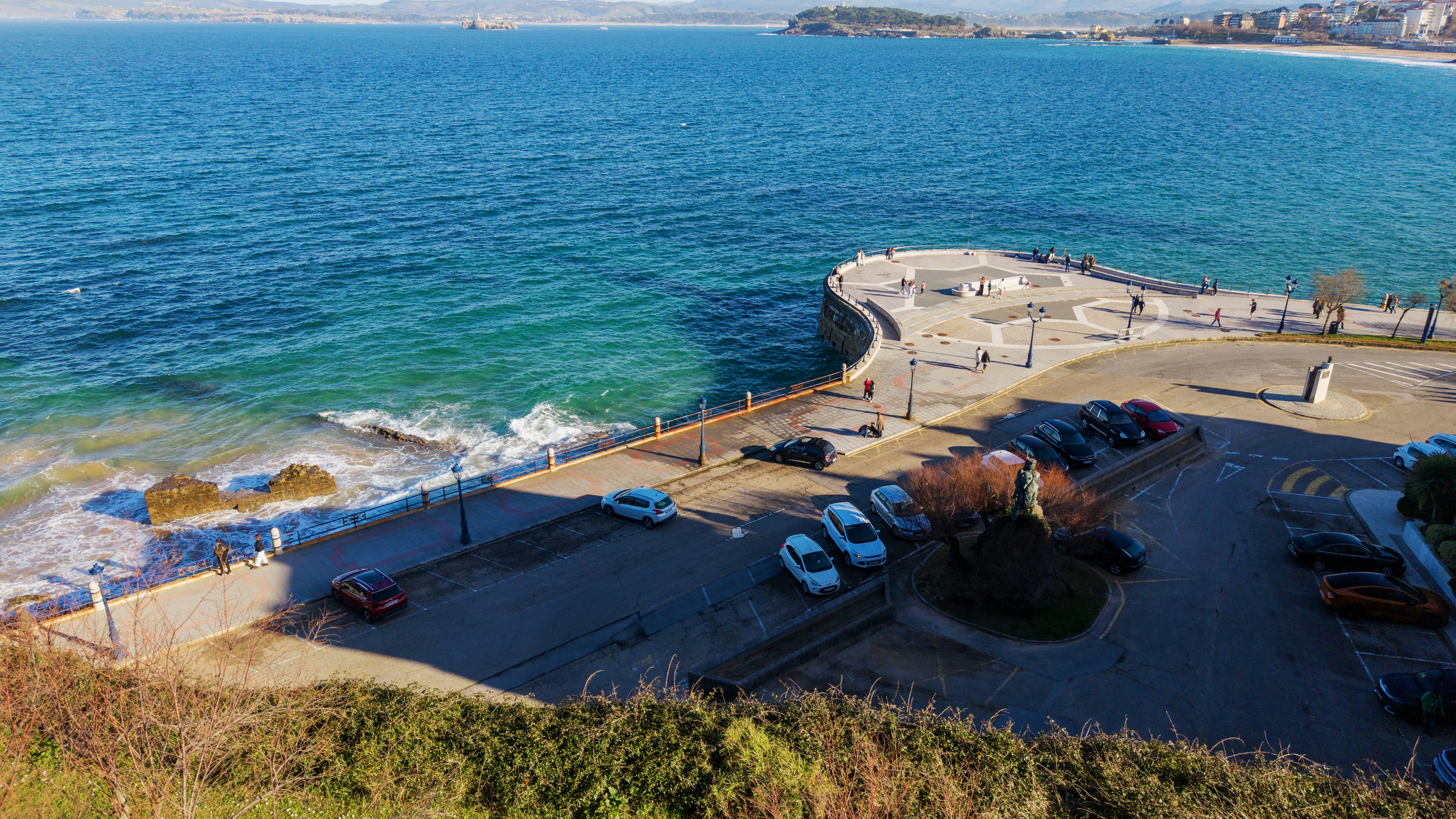 Cars parked near a coastal promenade overlooking the ocean.