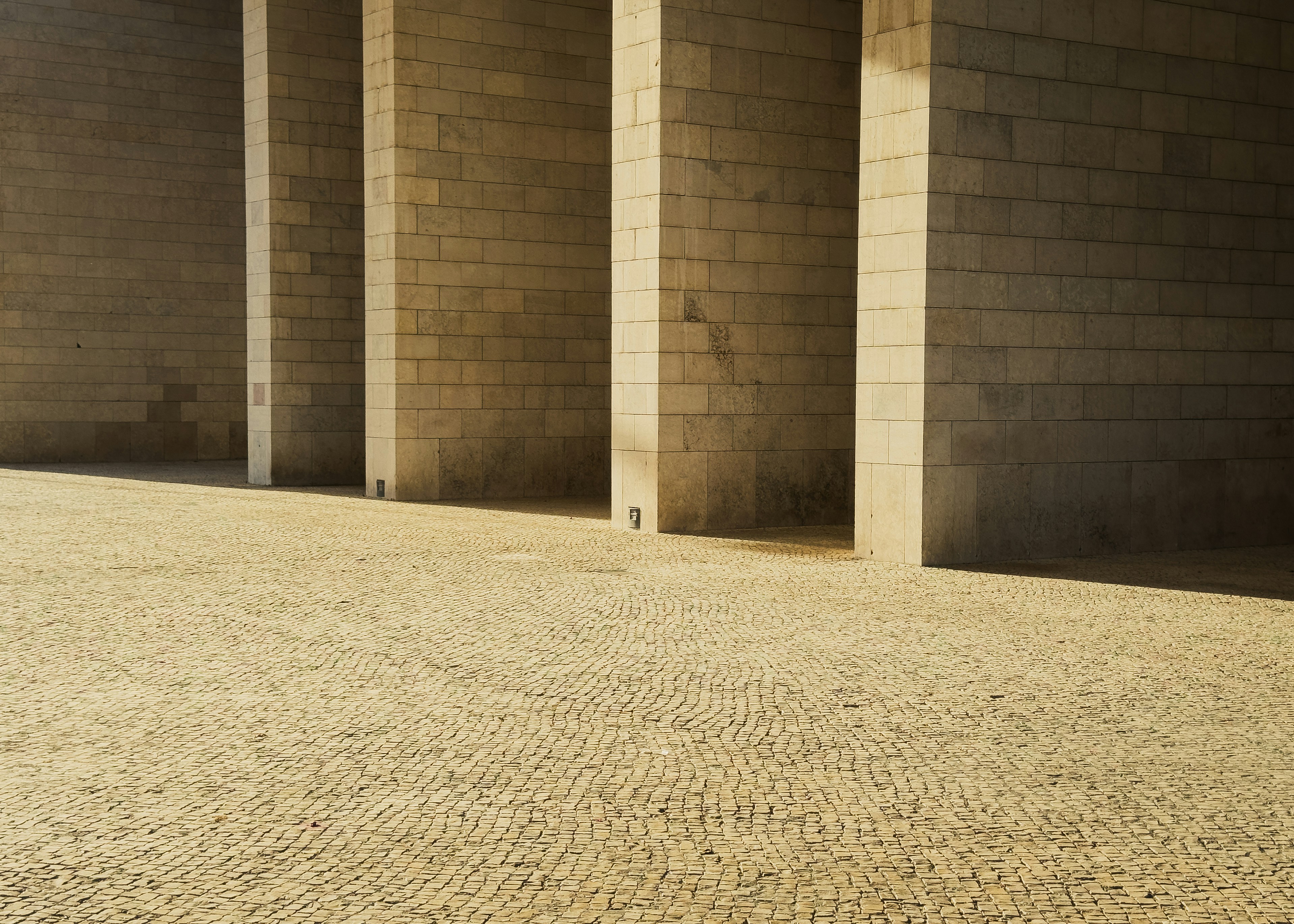 Stone columns casting shadows on a textured ground