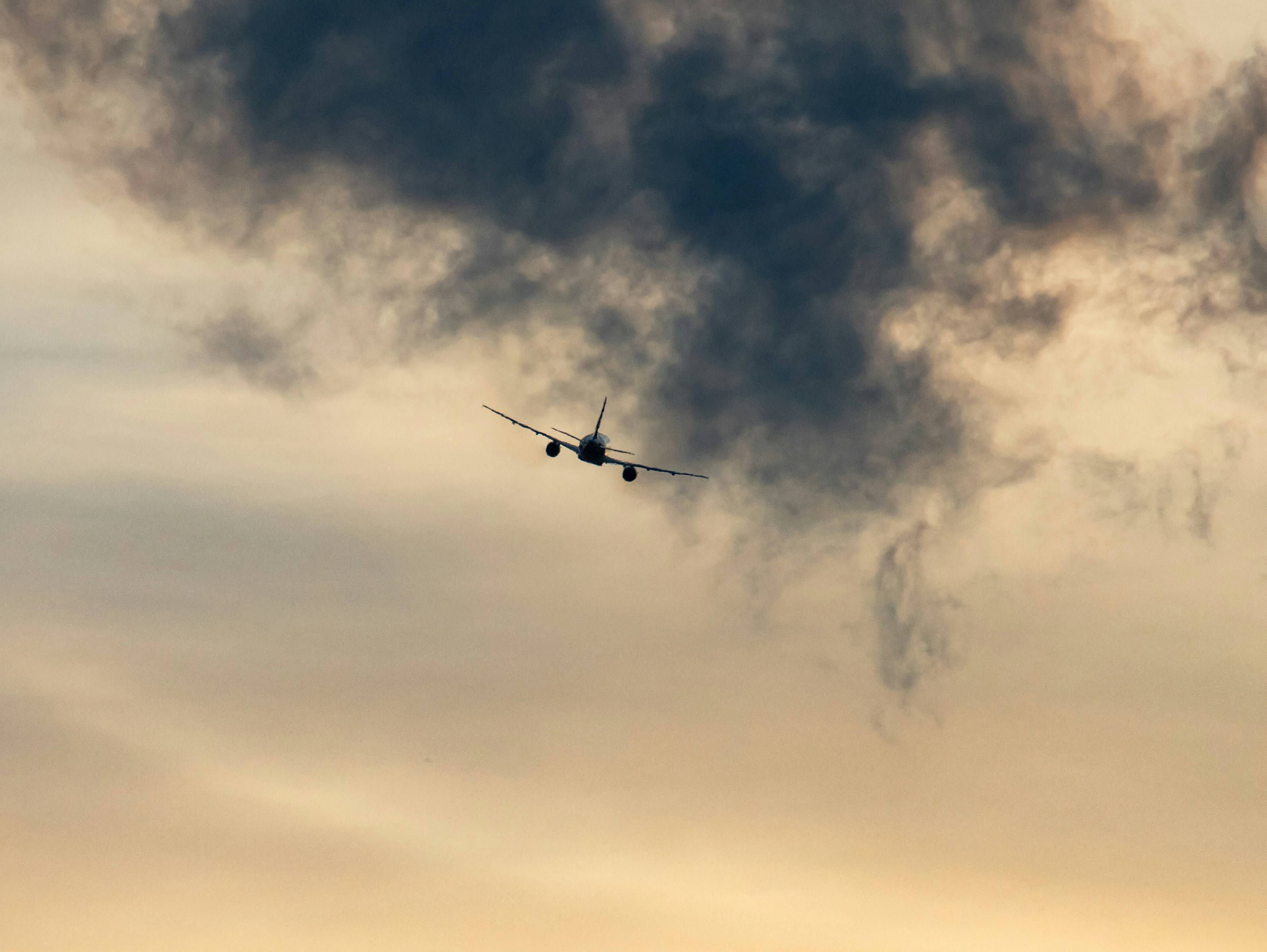 Airplane flying through dramatic clouds at sunset