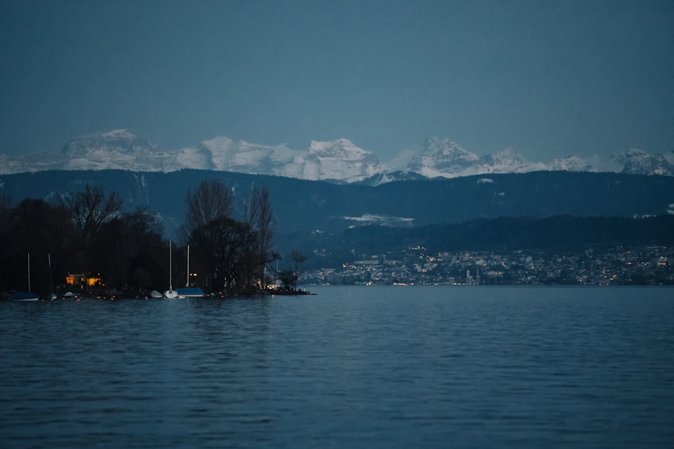 Serene lake surrounded by snow-capped mountains with small town at its base and boats on