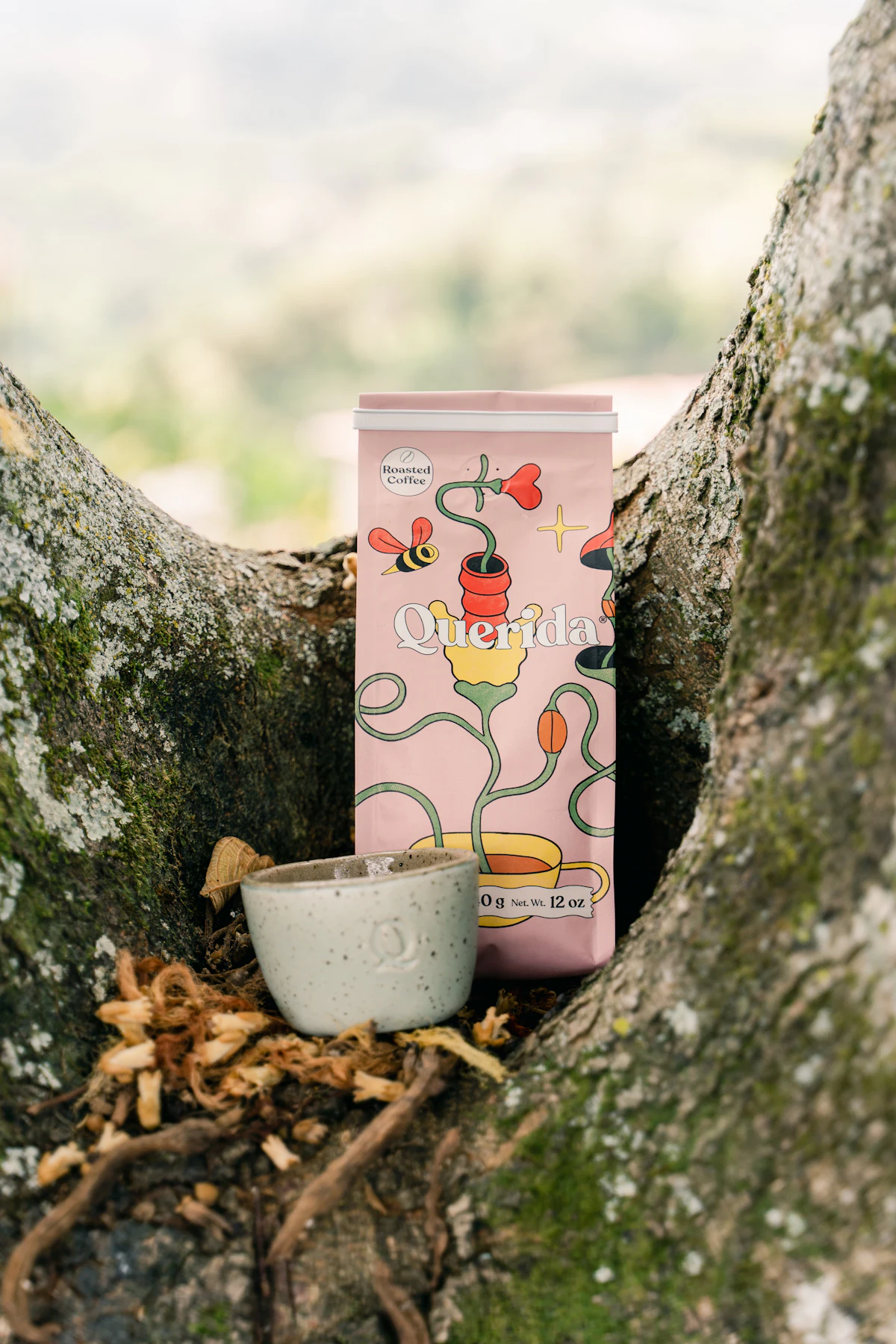 A small coffee cup and a pink coffee bag nestled in tree branches