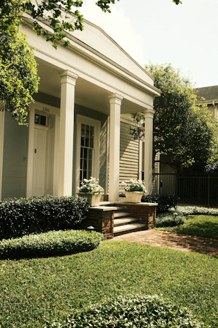A charming house with white columns and lush greenery.