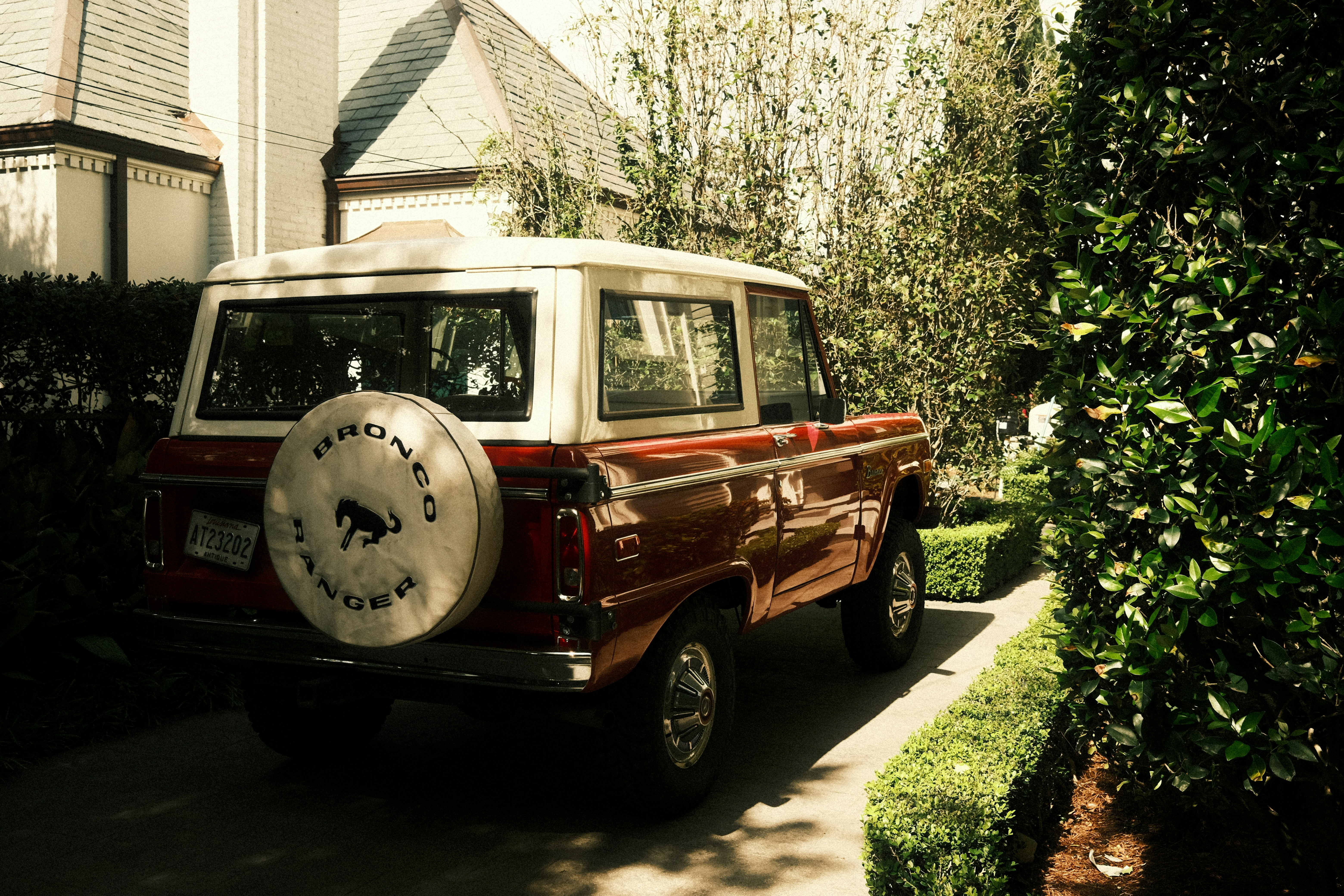 Un bronco rojo vintage aparcado en la entrada junto a la vegetación.