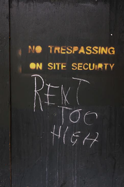 No trespassing sign with chalked message about rent.