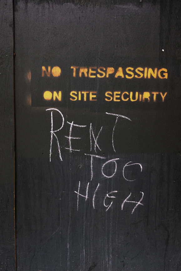 No trespassing sign with chalked message about rent.