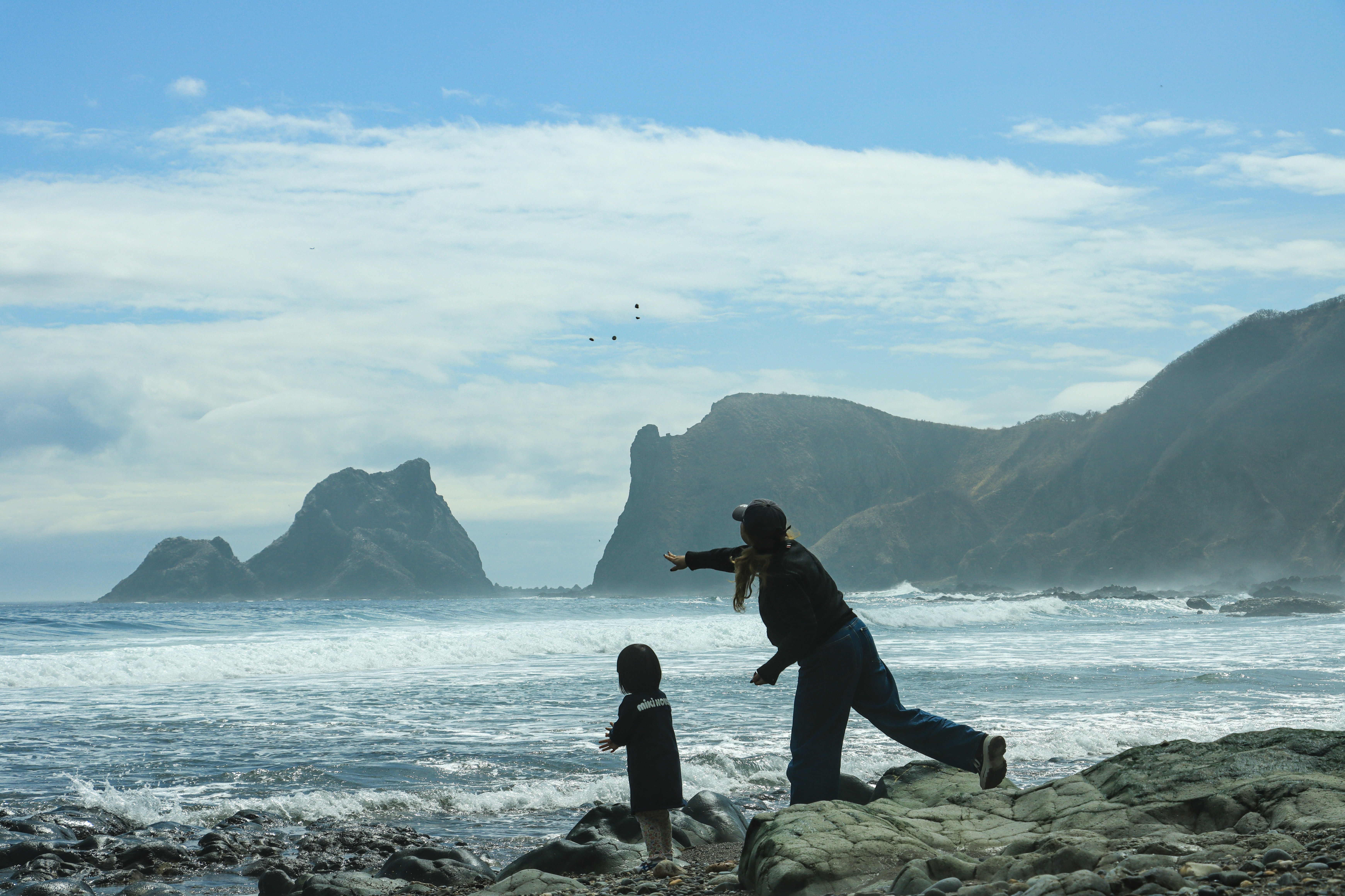 woman and child on a rocky coast with waves