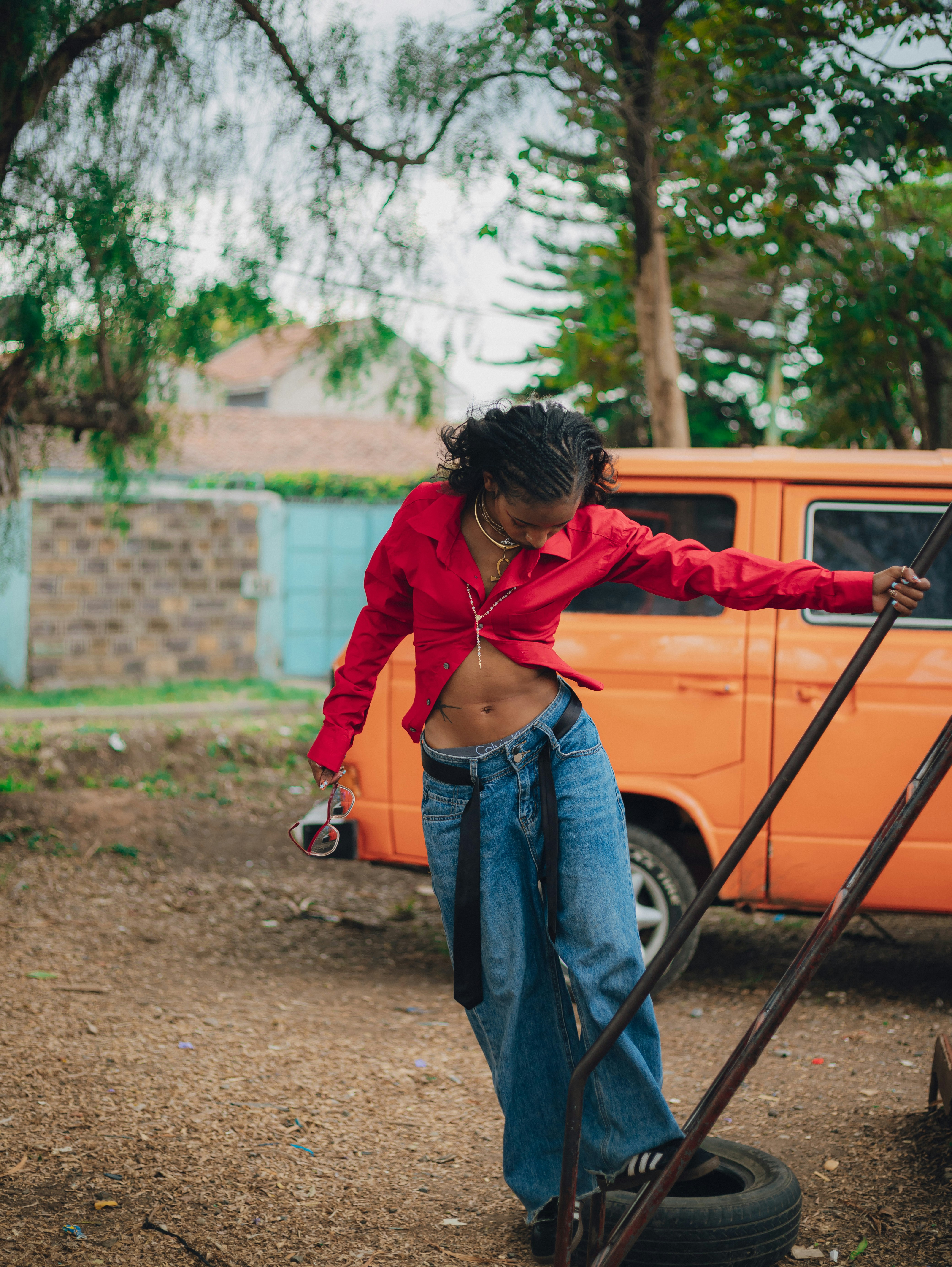 Mujer con camisa roja y vaqueros anchos sostiene la cámara.