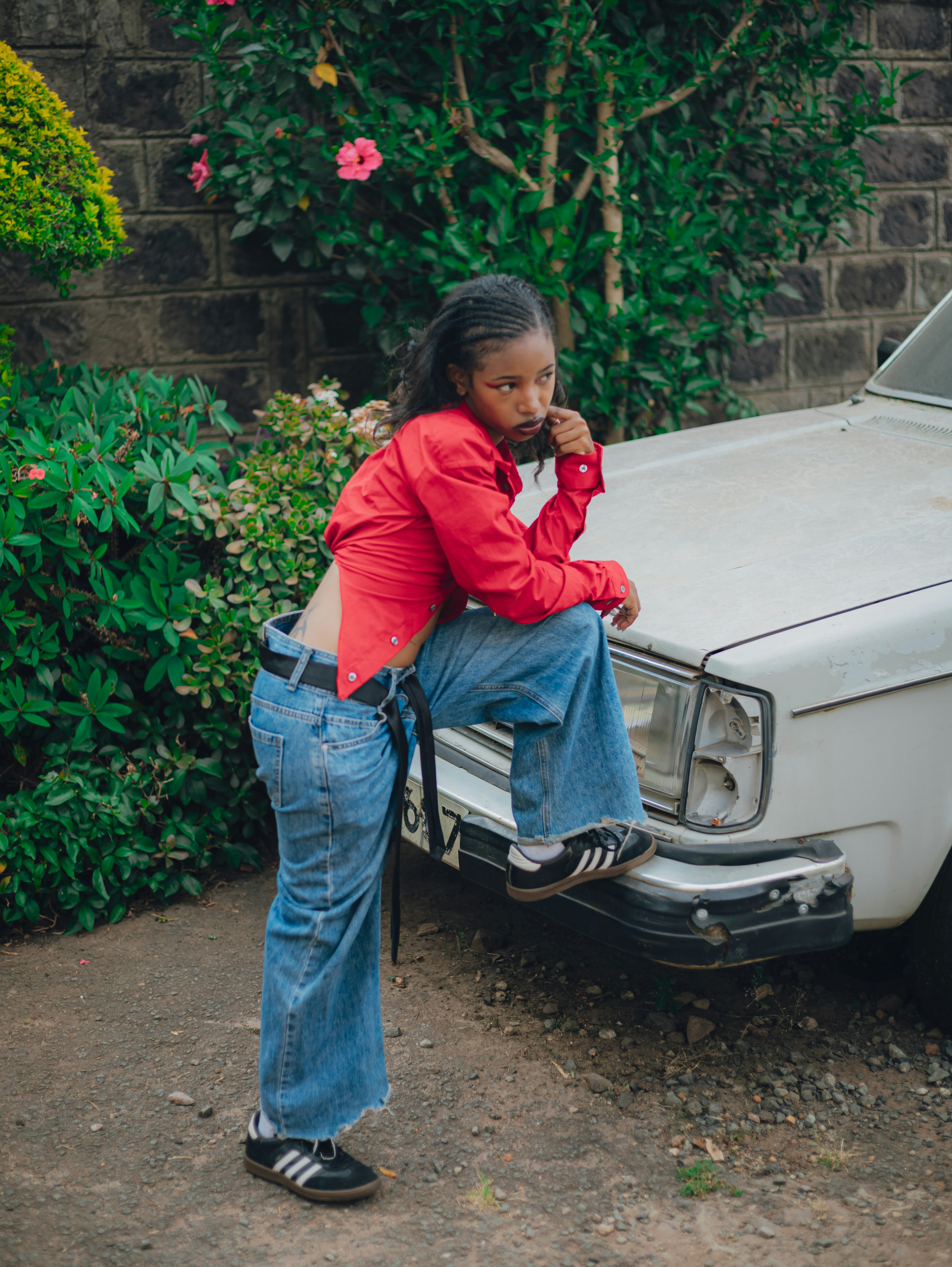 Junge Frau im roten Hemd und Jeans lehnt sich an das Auto