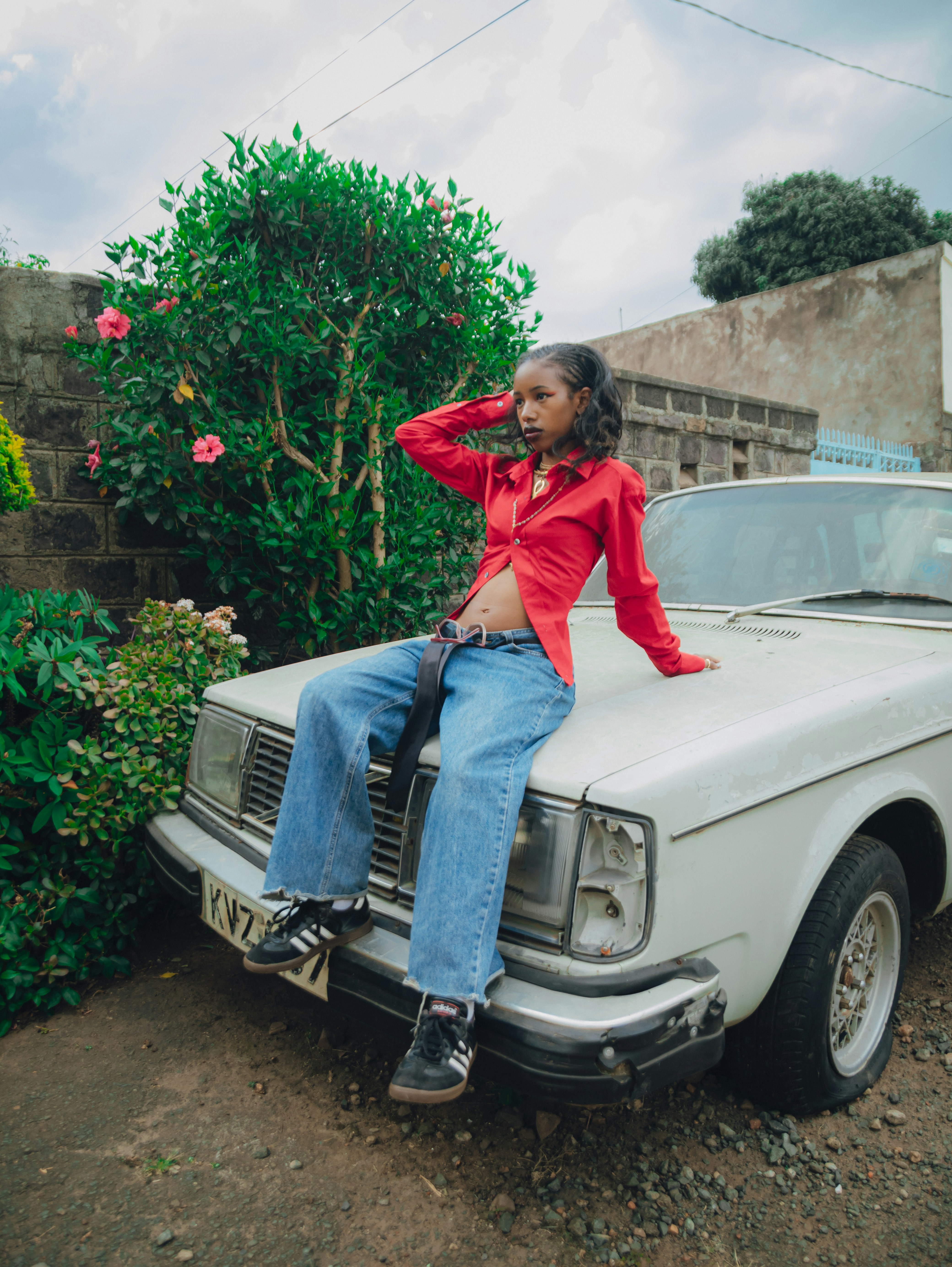 Frau im roten Hemd und Jeans sitzt auf der Motorhaube.