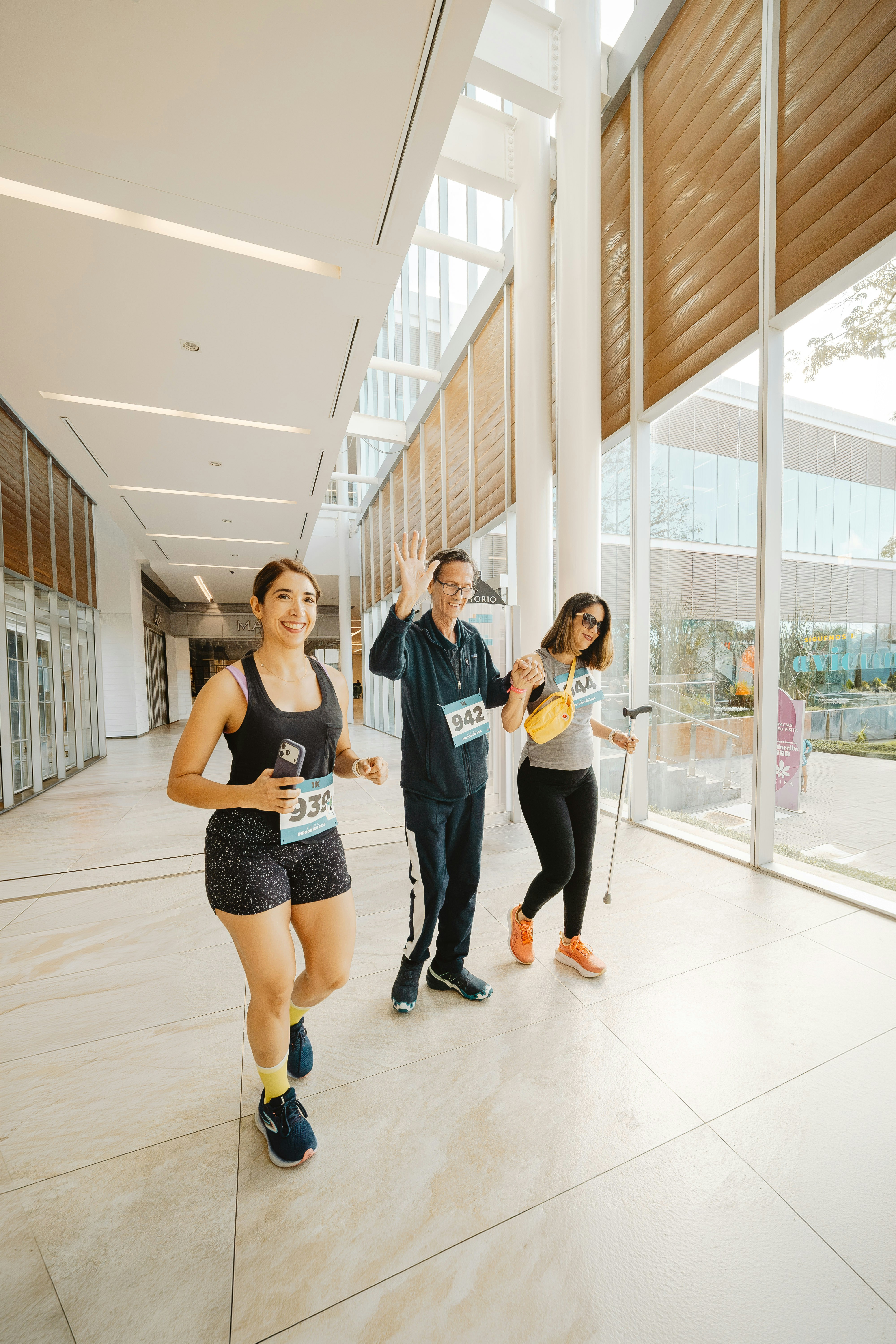 Three people walking in a bright hallway with windows