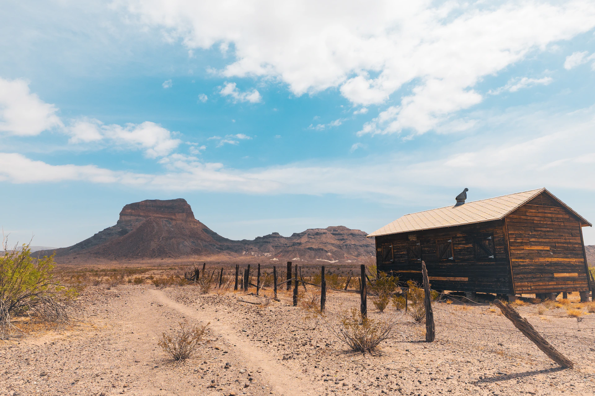 Rustic wooden cabin in a desert landscape with mountains.
