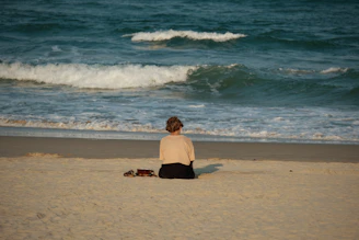 Woman sitting on beach facing the ocean waves