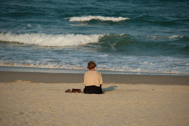 Woman sitting on beach facing the ocean waves