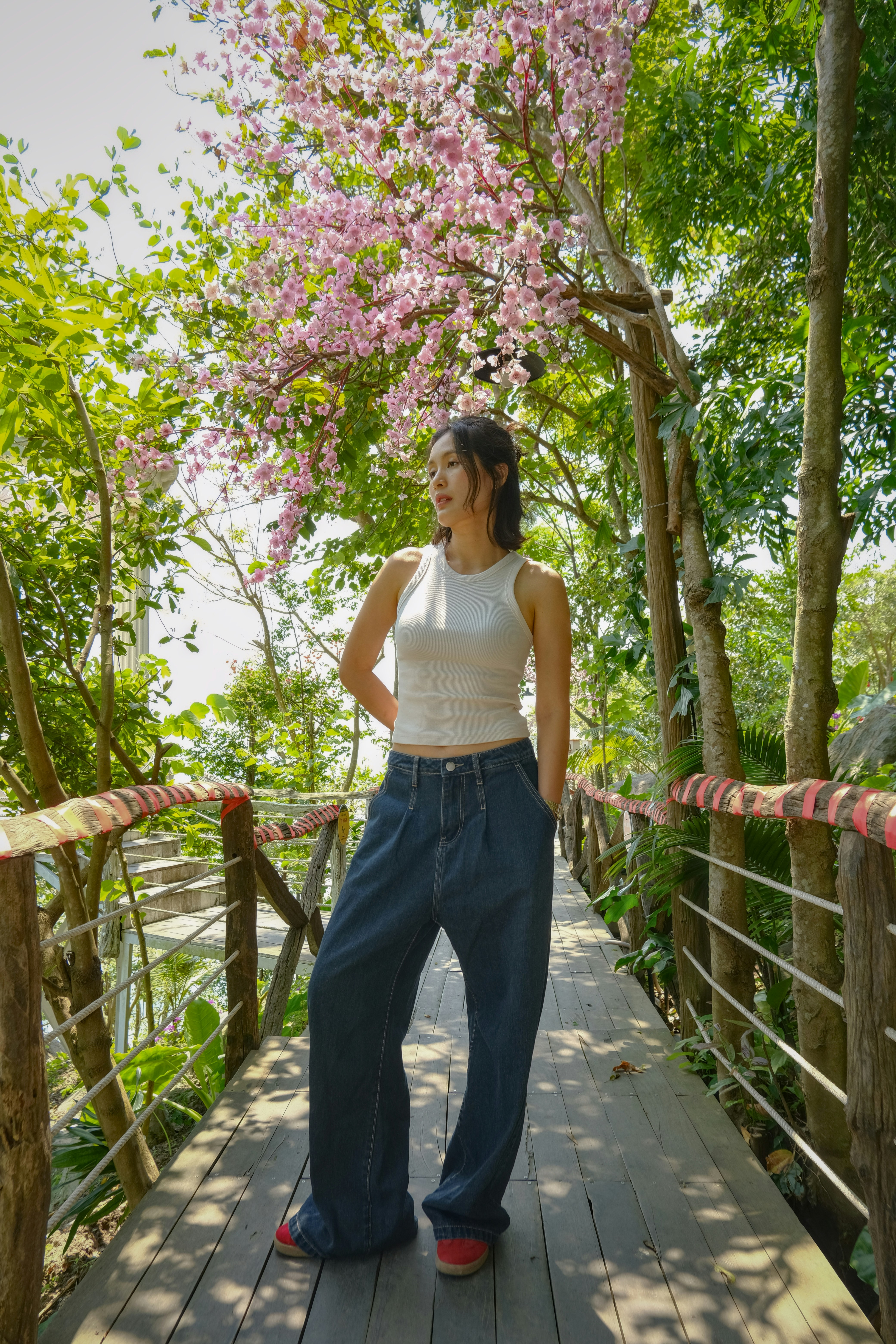 A woman stands on a wooden bridge under blooming trees.