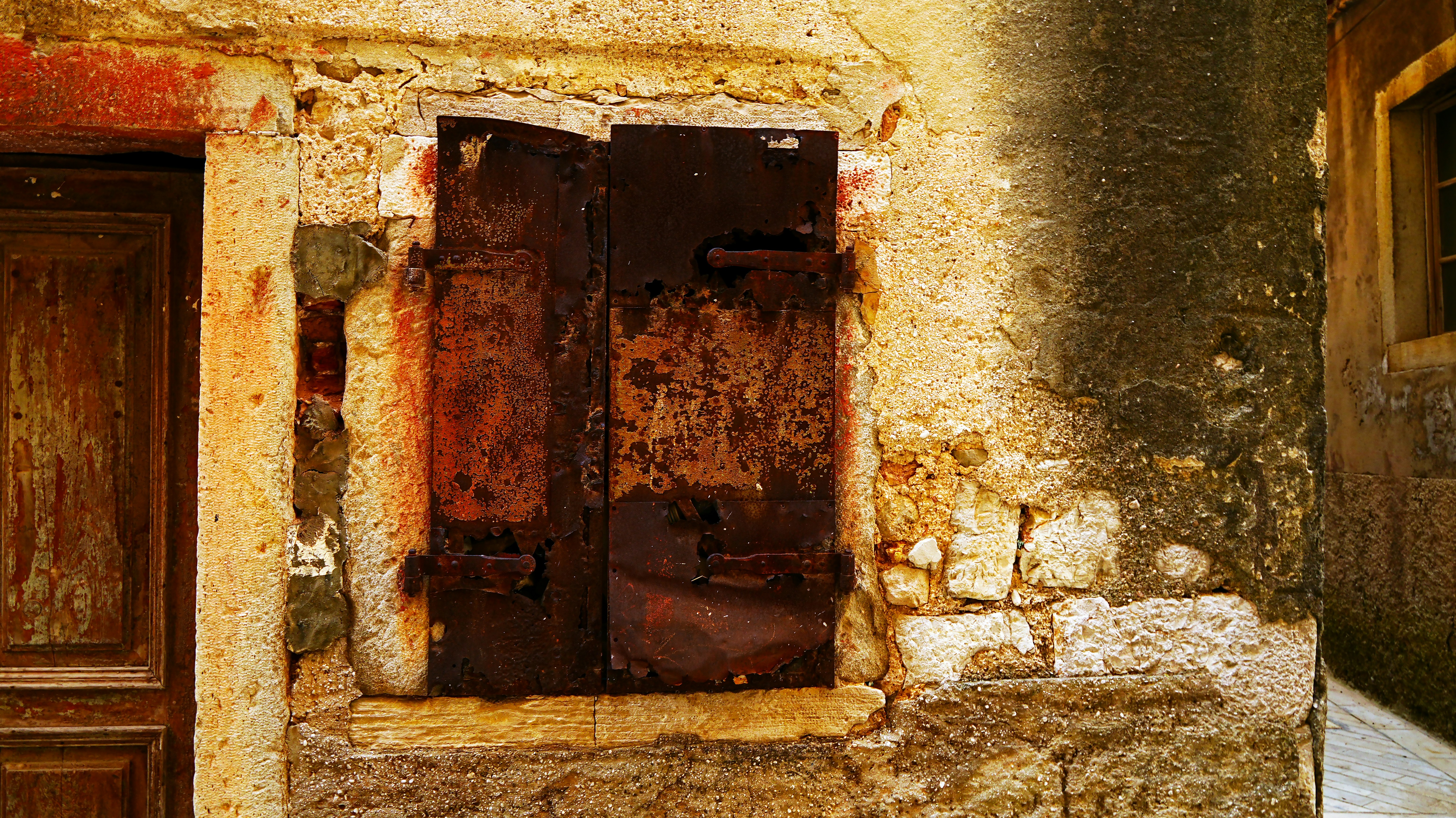 Une porte métallique usée et rouillée, encastrée dans un mur de pierre.