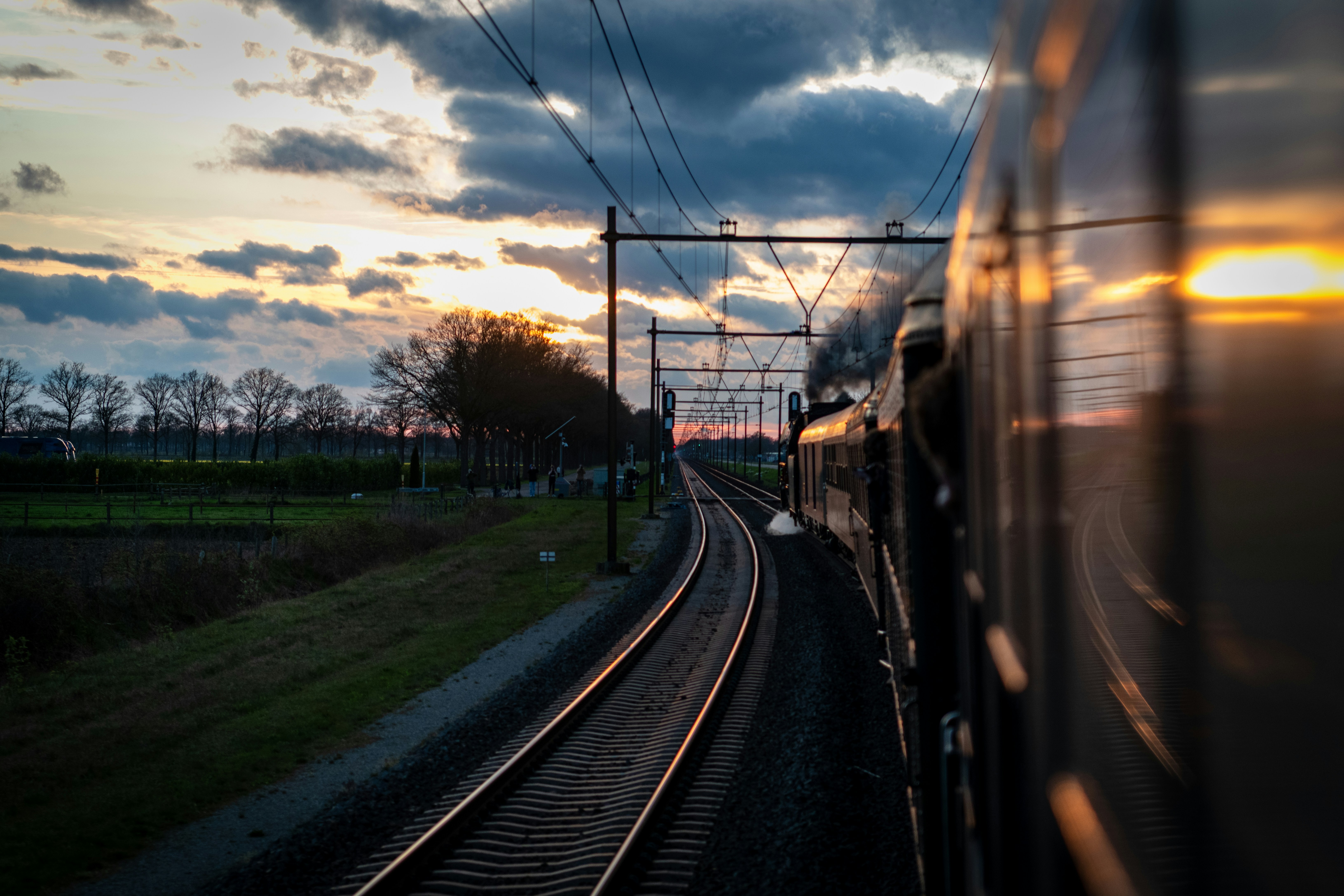 Train traveling on tracks during sunset with dramatic clouds.